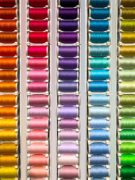 File verticali di rocchetti di filo da cucito colorati, disposti in una sfumatura dall'alto verso il basso.
