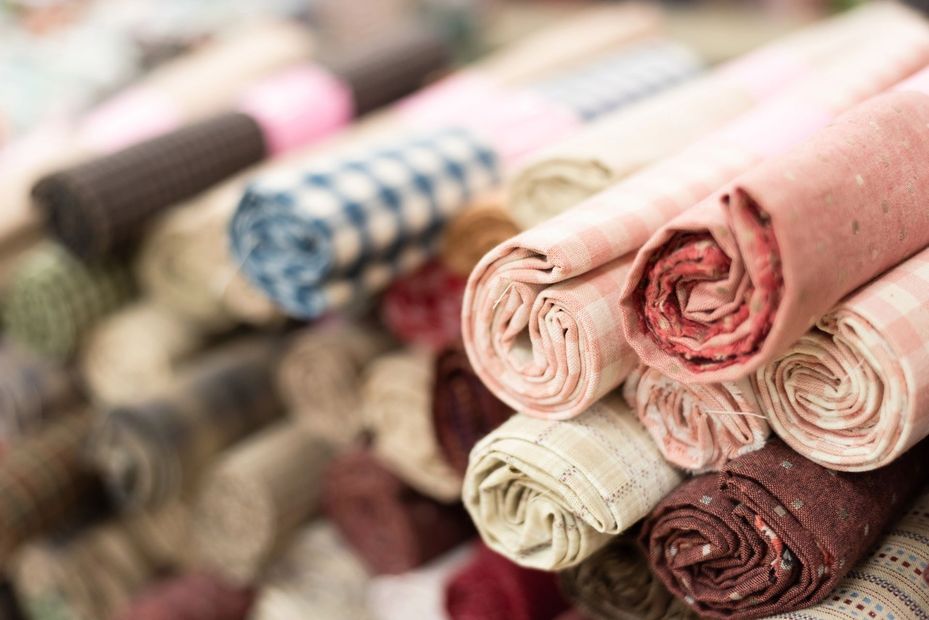 In una ripresa ravvicinata e angolata, si vedono diversi rotoli di tessuto multicolore e dalla trama particolare, impilati uno sull'altro.