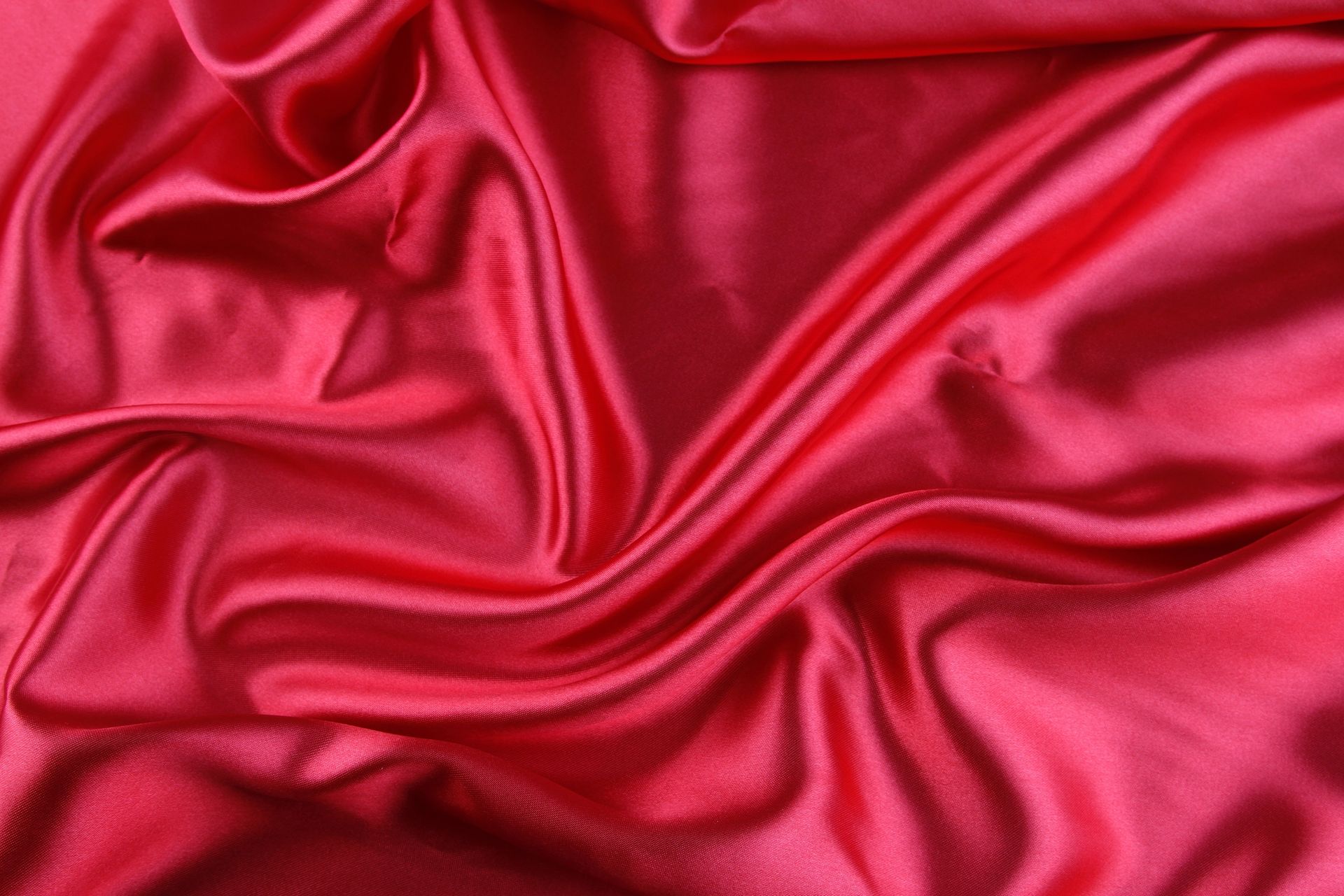 Tessuto di raso rosso con morbide pieghe e riflessi.