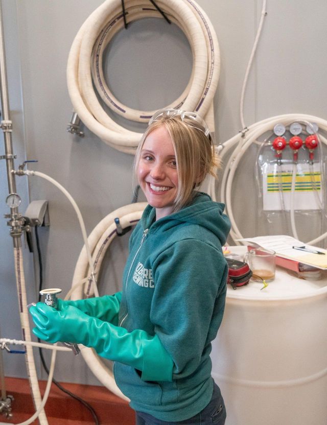 A woman wearing green gloves and a green hoodie is standing next to a barrel.