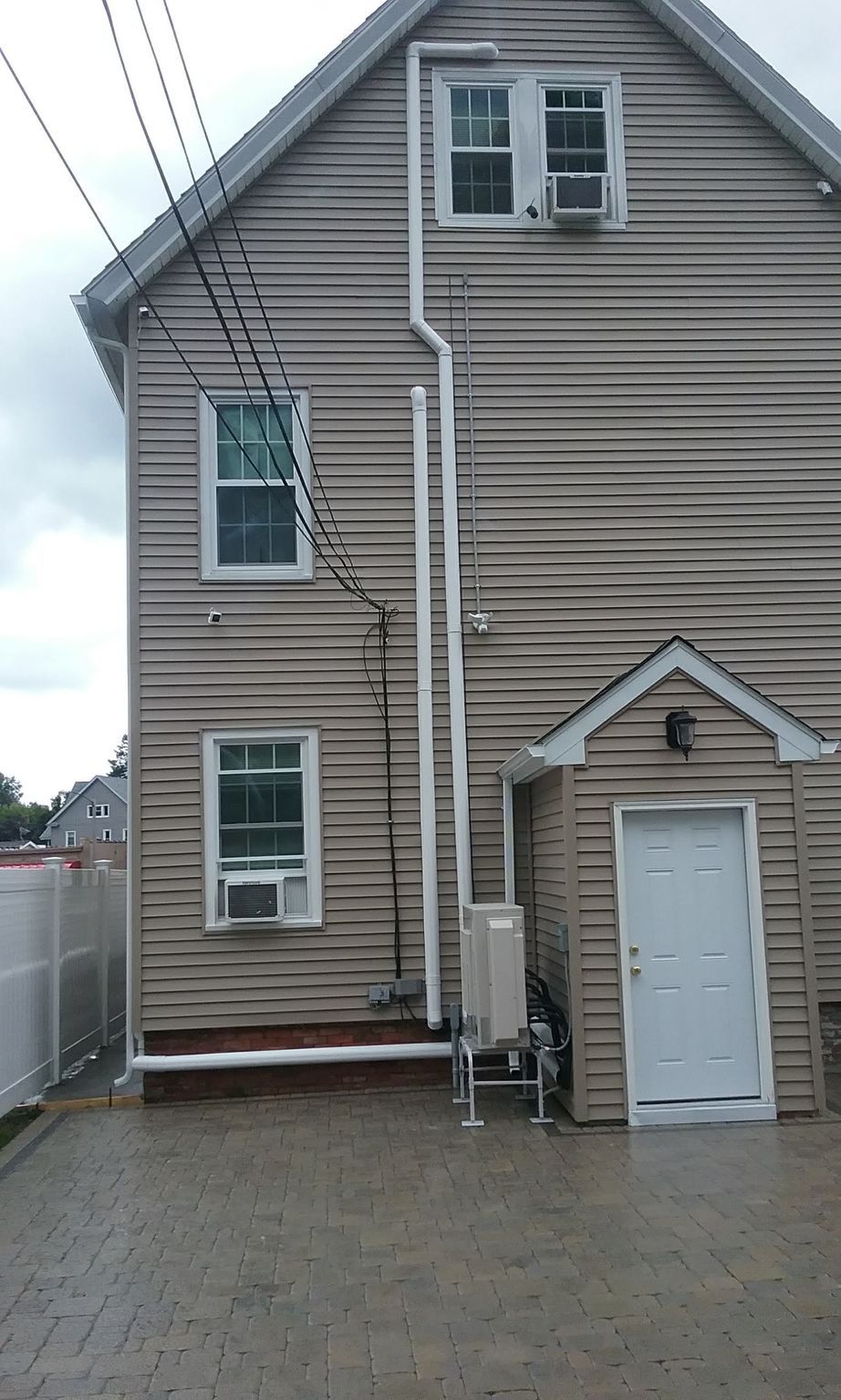 Side view of a two-story house with tan siding and a small attached garage, featuring windows and power lines.