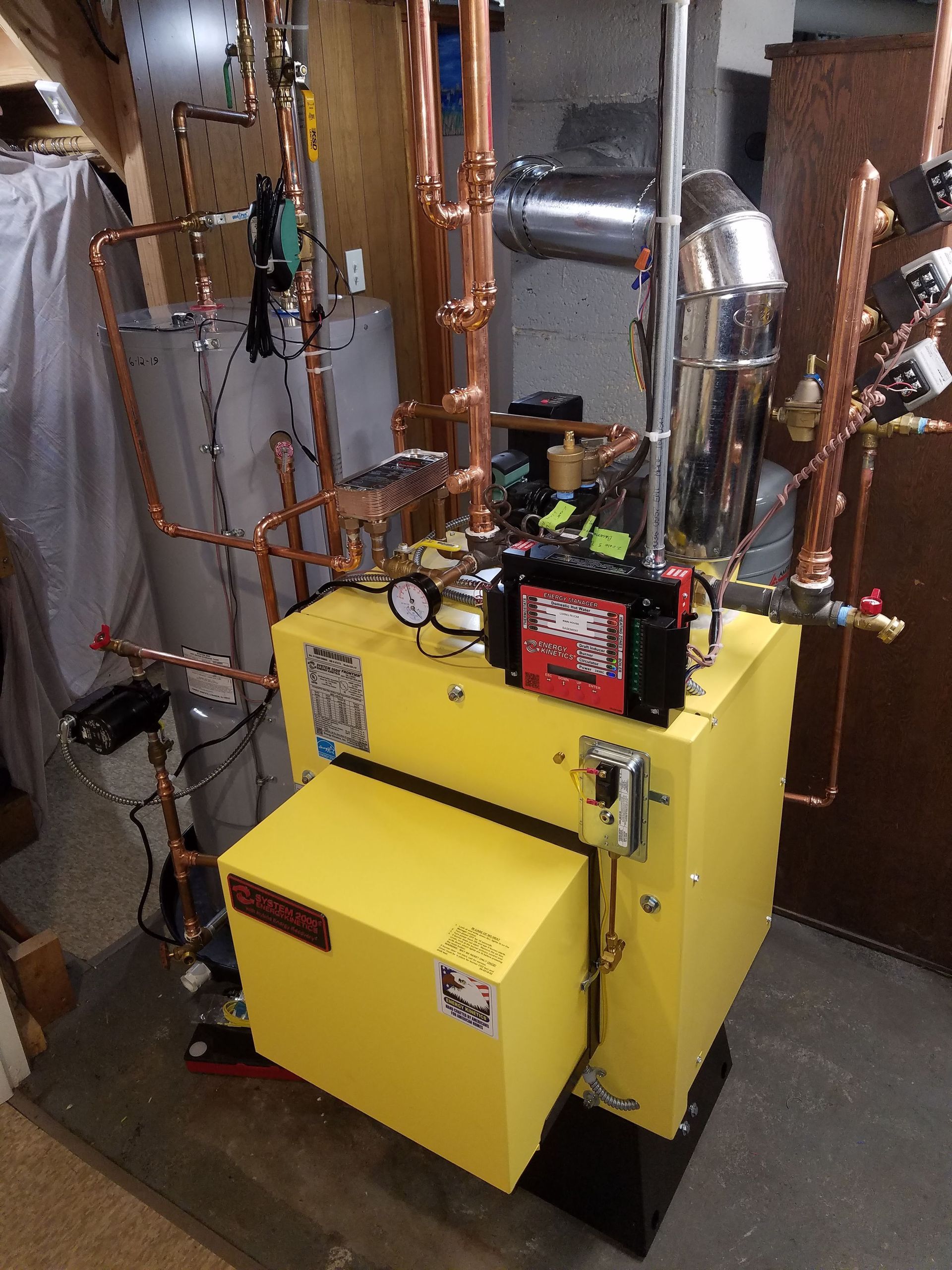 Yellow furnace with copper pipes, gauges, and controls in a basement setting.