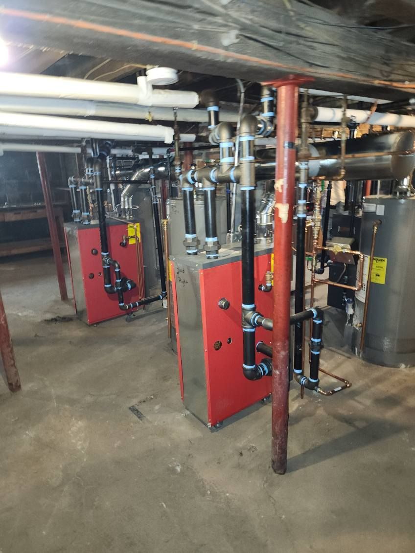 Two red heating boilers with black pipes in a basement, supported by a red beam.