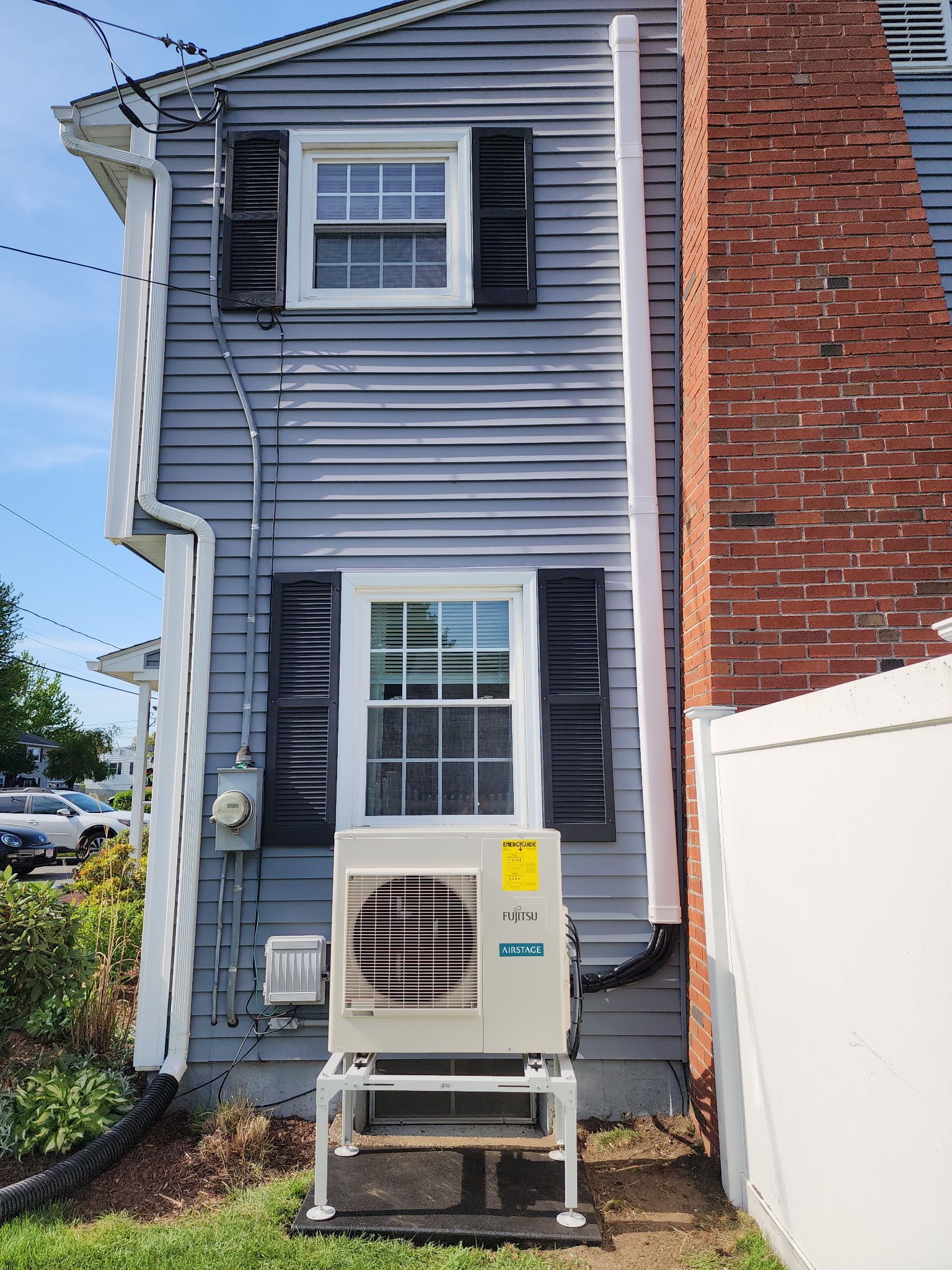 Side of a blue house with an air conditioning unit on a raised platform, beside a chimney and a white downspout.