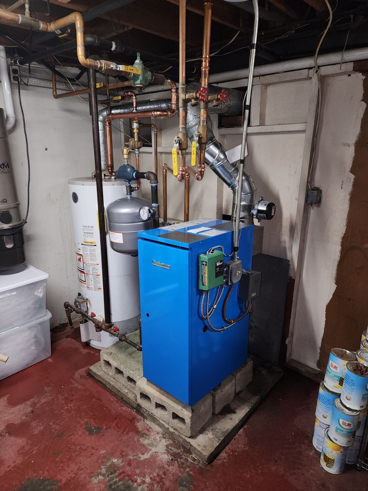 Blue furnace and white water heater in a basement, surrounded by copper pipes and storage containers.