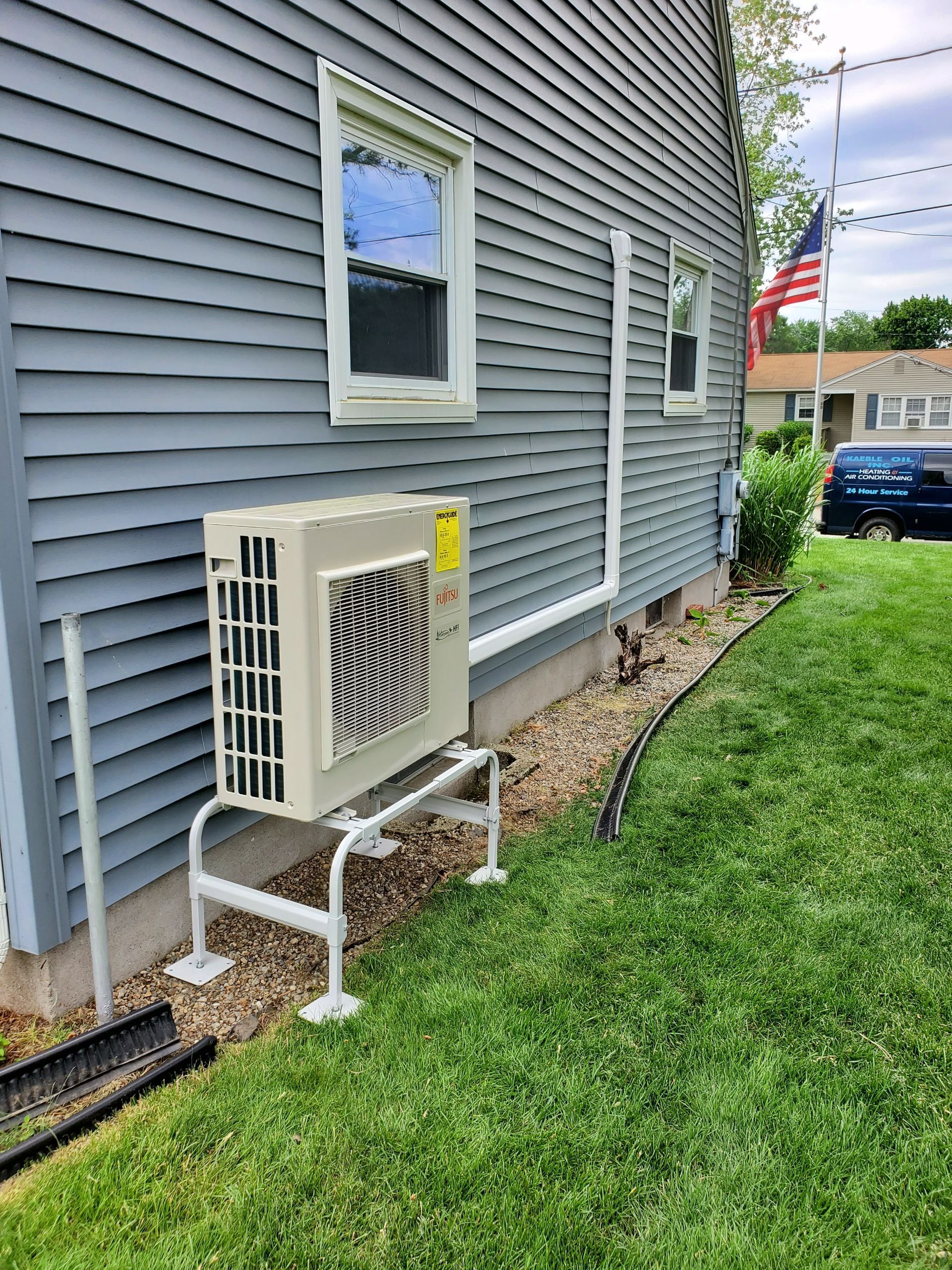 Exterior view of a gray house with a mounted air conditioning unit on a metal stand.