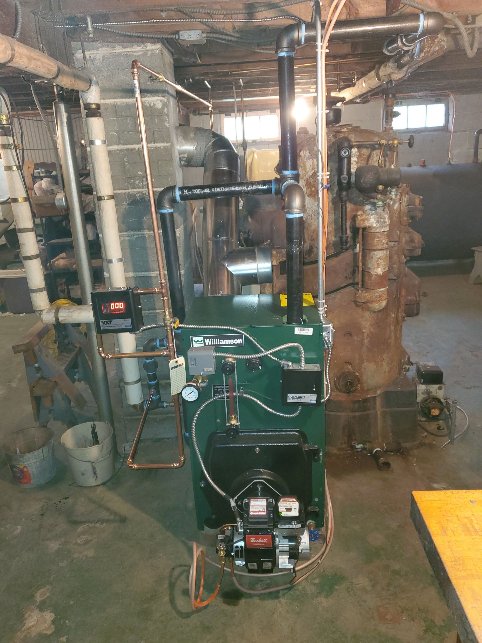 Green furnace with black pipes in a basement.