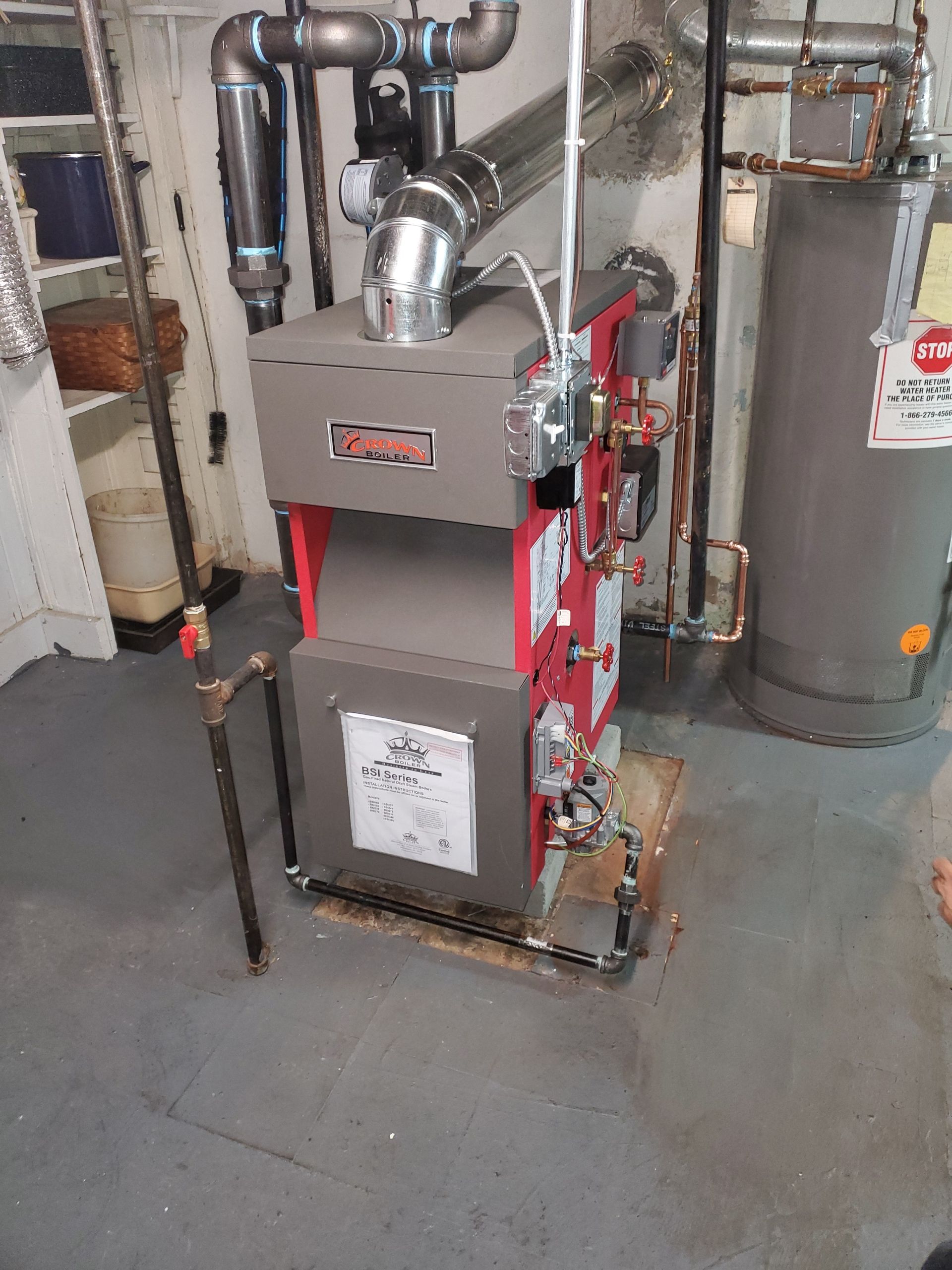 Red and gray furnace in a basement, with pipes and a water heater visible.
