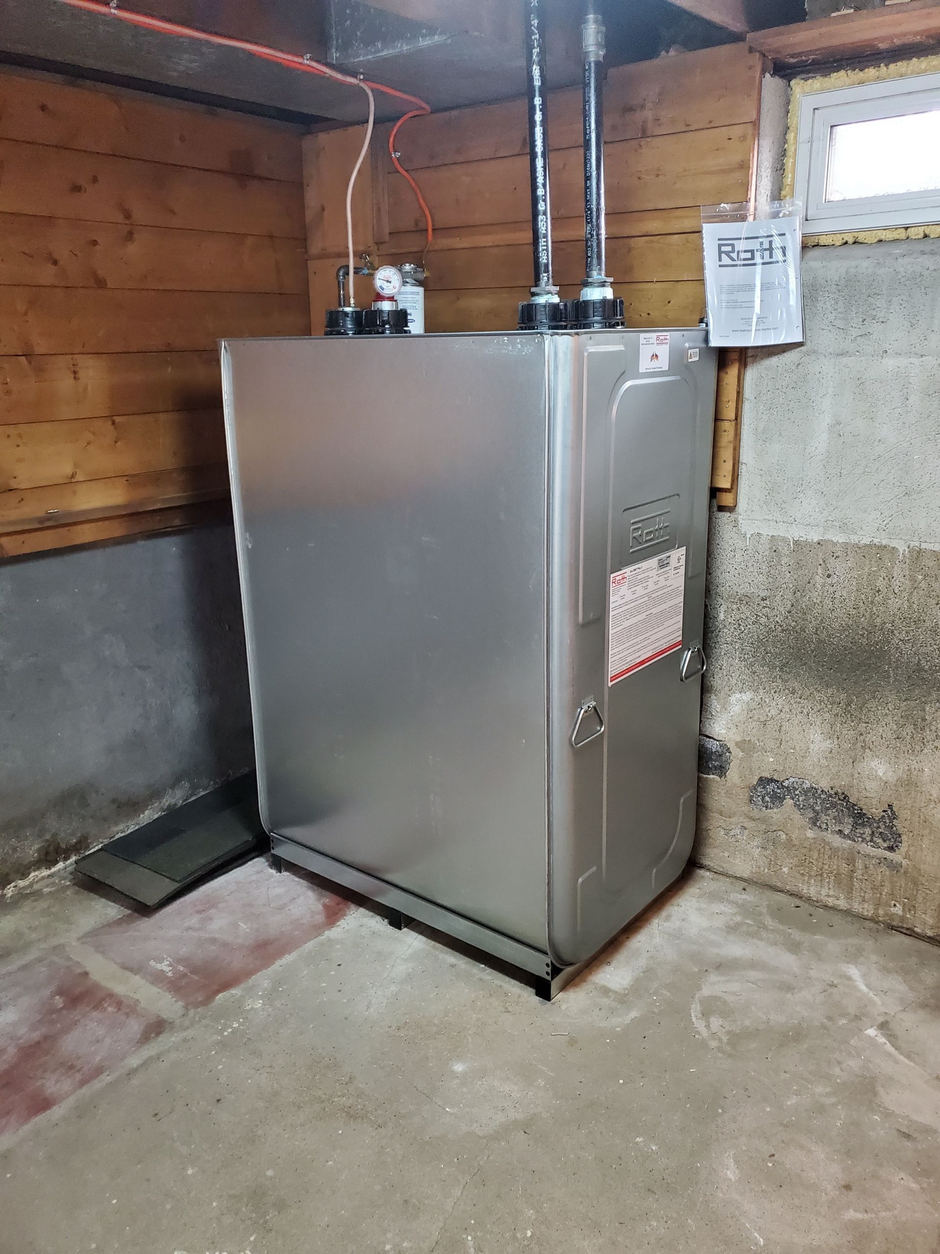 Silver furnace in a basement corner with pipes and wires.