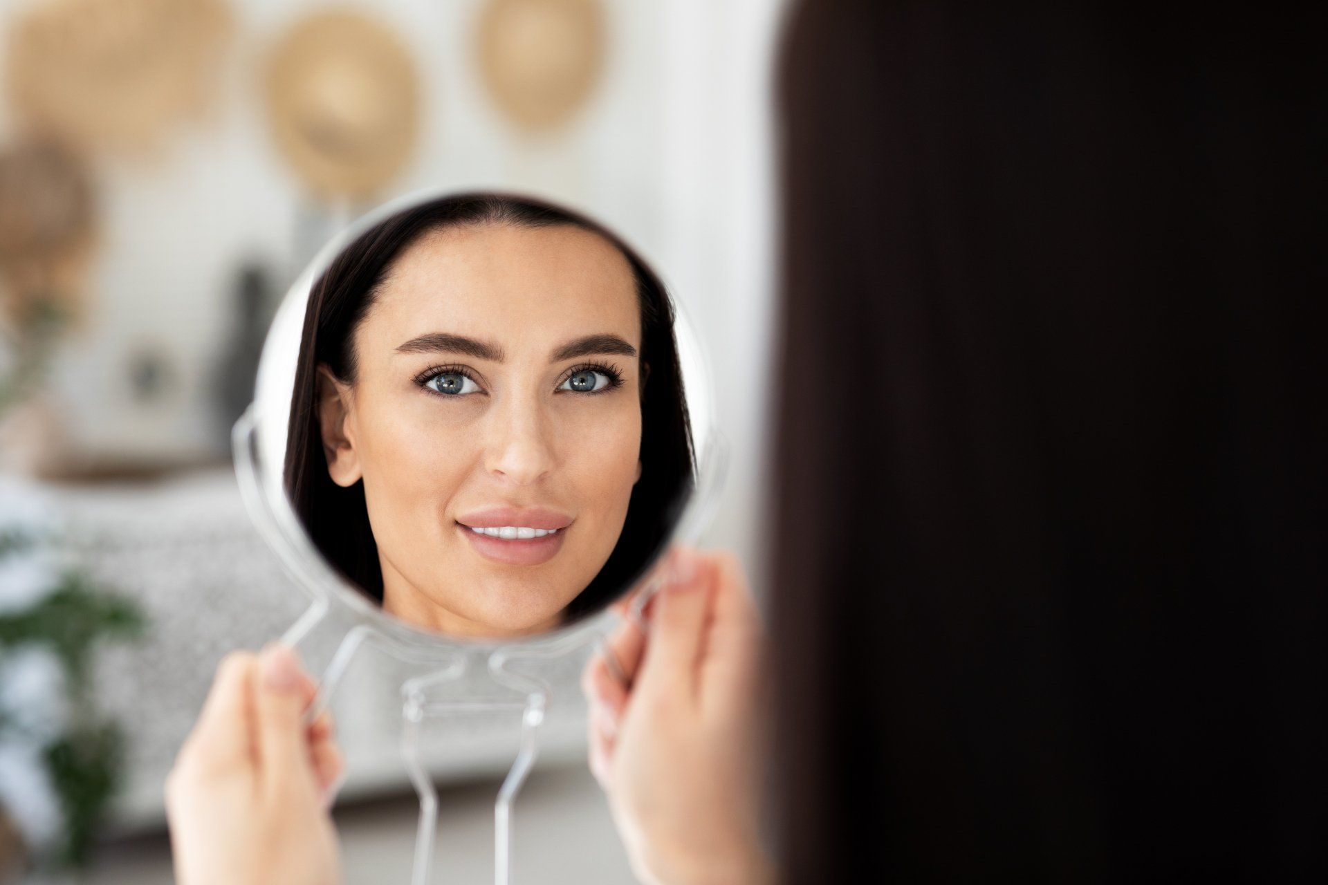 brunette woman looking at her reflection in a hand held mirror