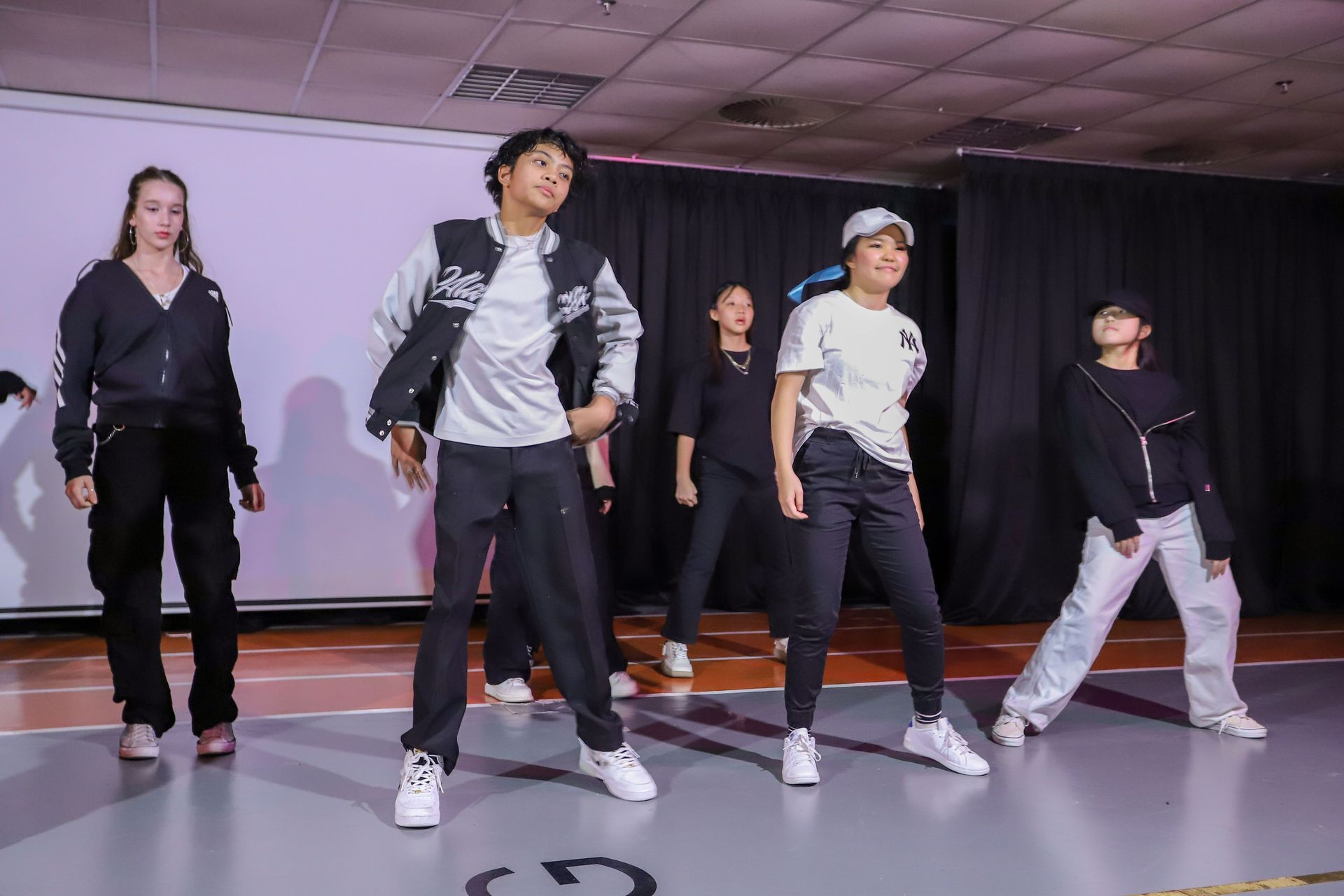 Group of dancers performing on a stage. They wear casual clothes, and are in motion.