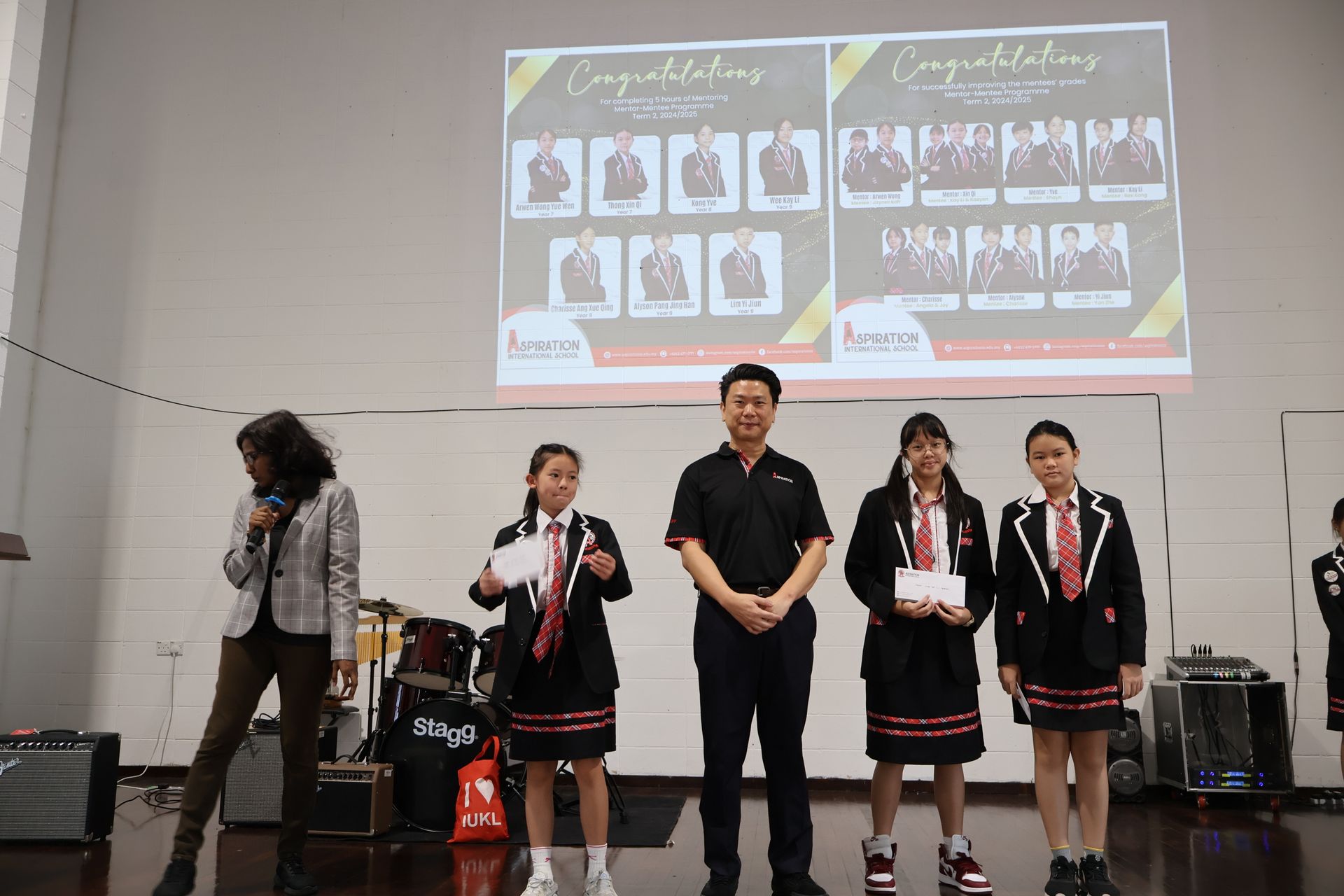 People on stage with certificates and a projector screen displaying photos.