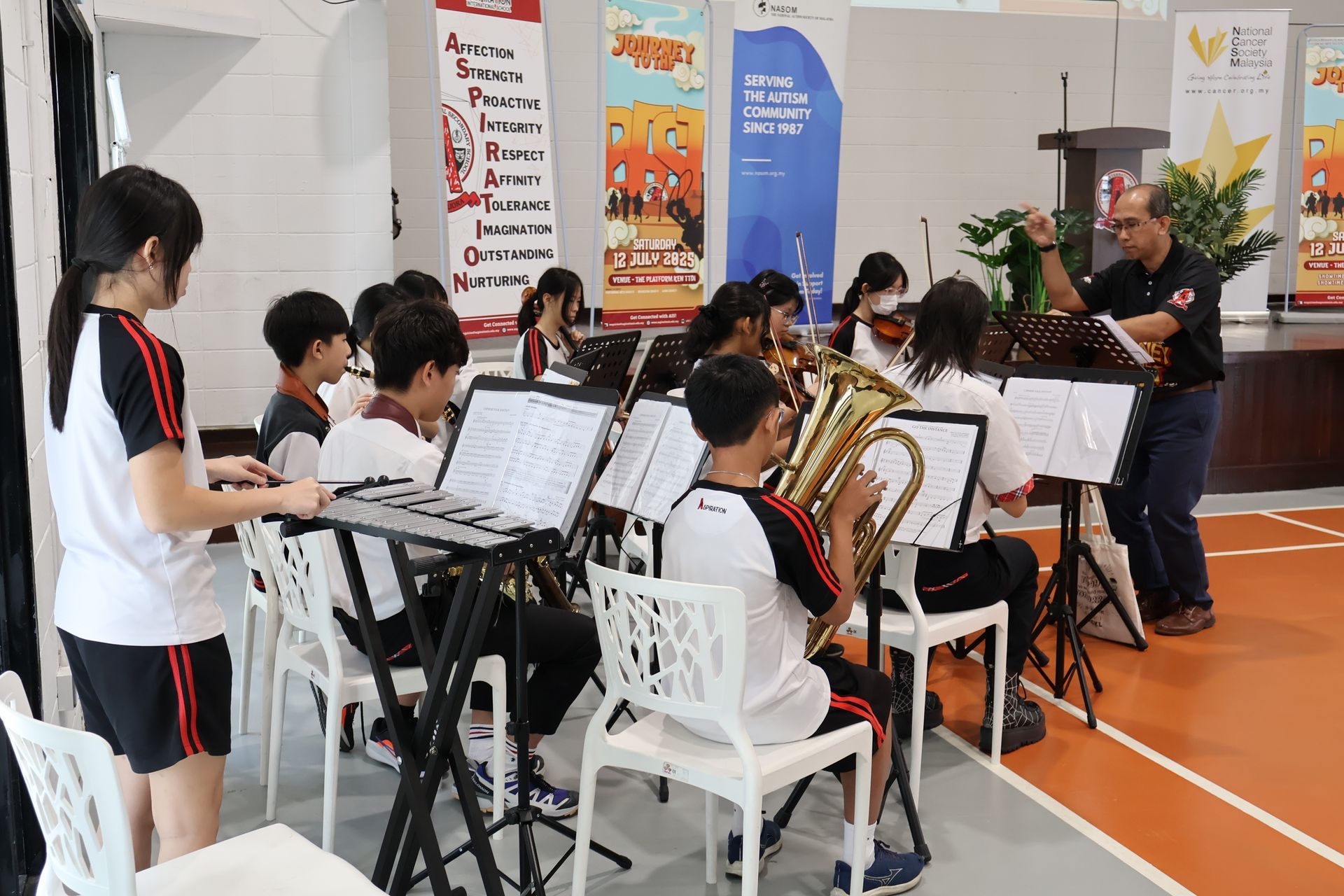 A school band rehearsing. Students play instruments as a conductor directs in a gymnasium.