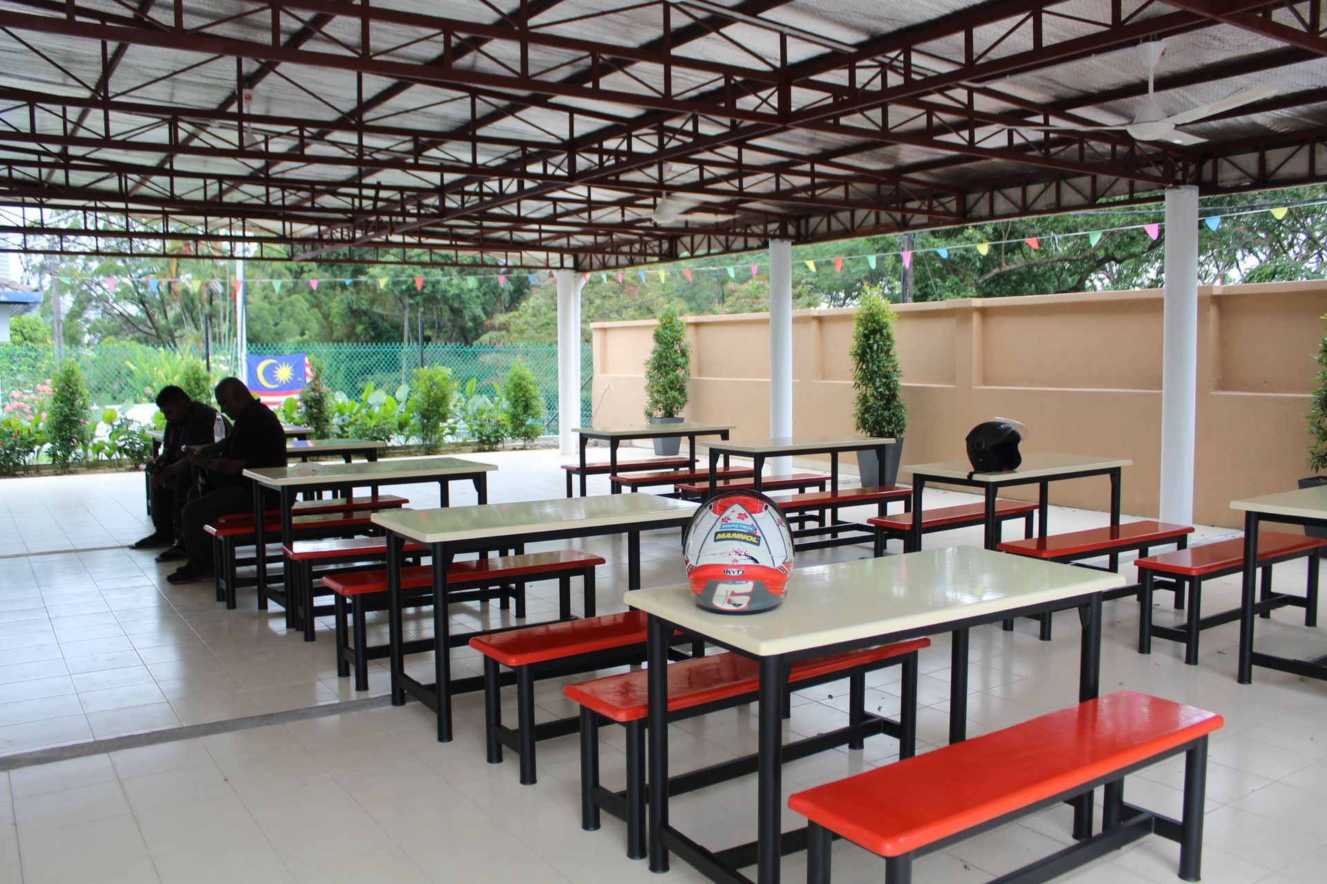 Outdoor covered dining area with tables and benches. Two people sit at a table.