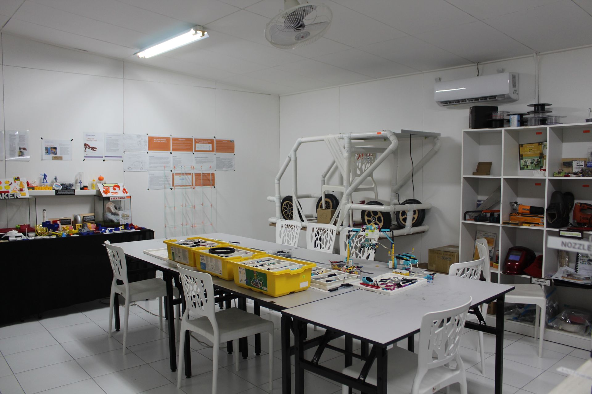 A well-lit workshop with a table holding LEGOs, a white wheeled cart, and shelves with materials.