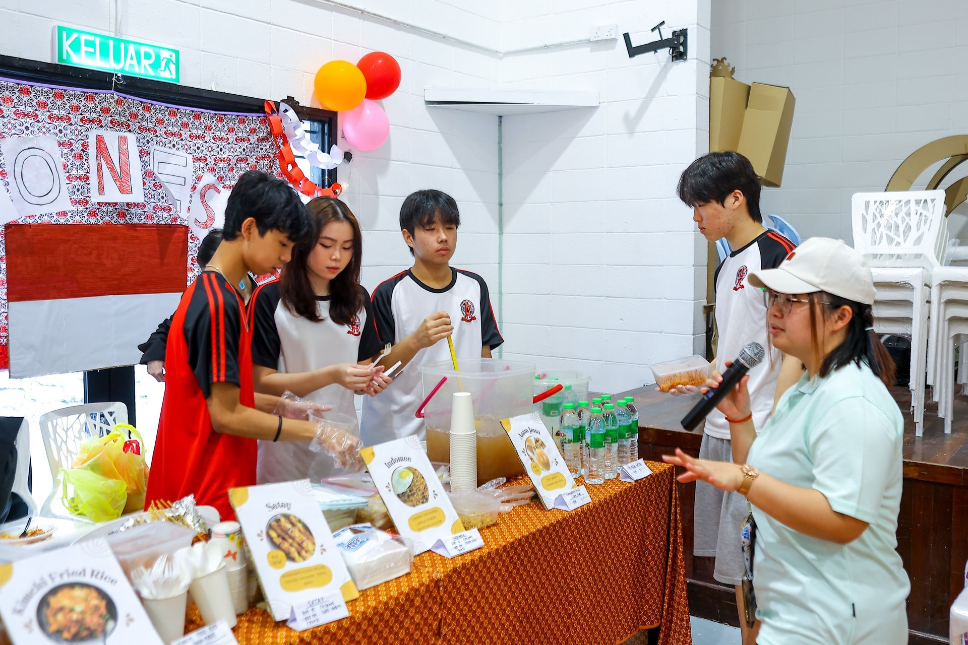 People at a food stall with Indonesian flags and decor. Several people are buying or serving food.
