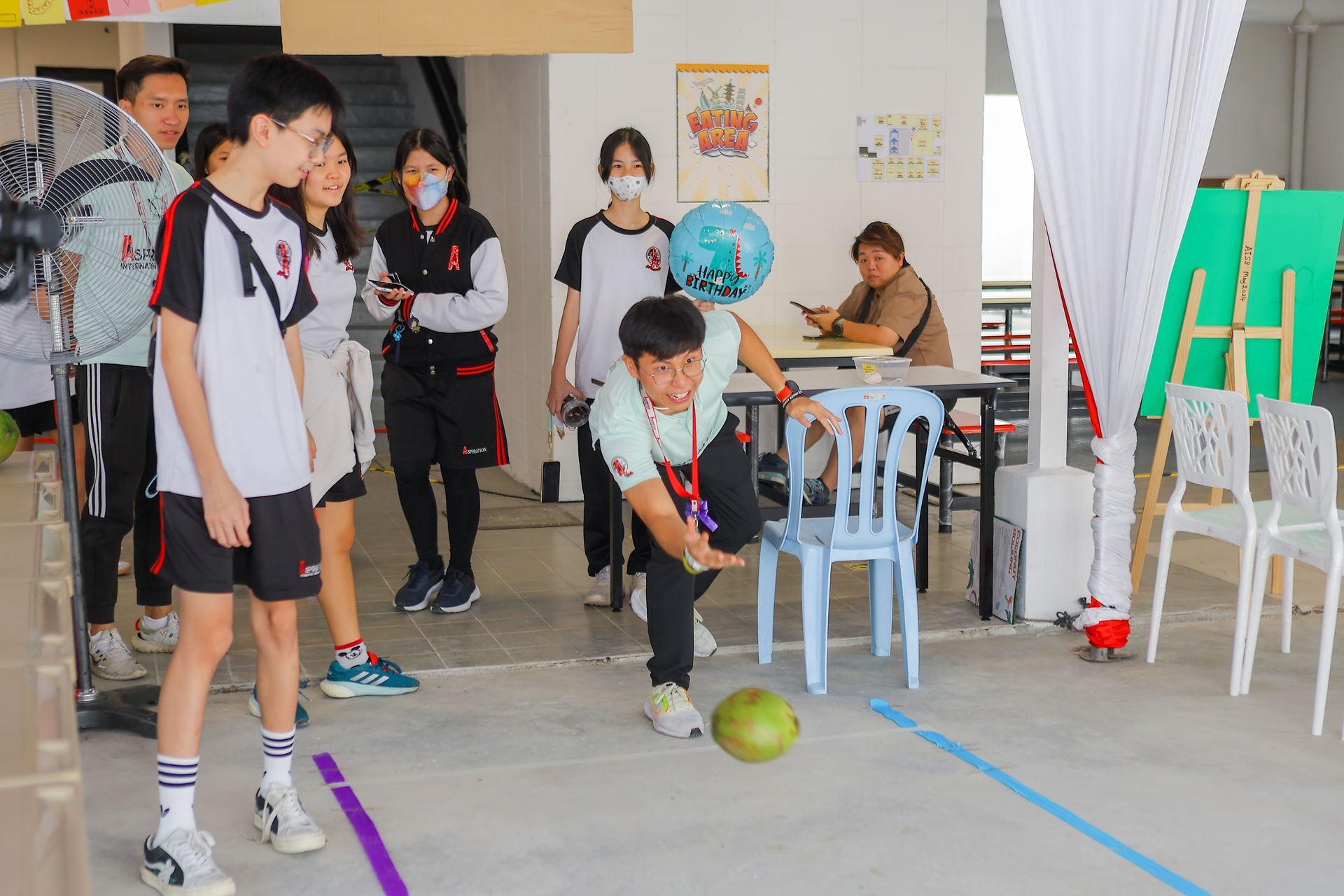 A person kicking a ball towards a line, observed by several people in a room.