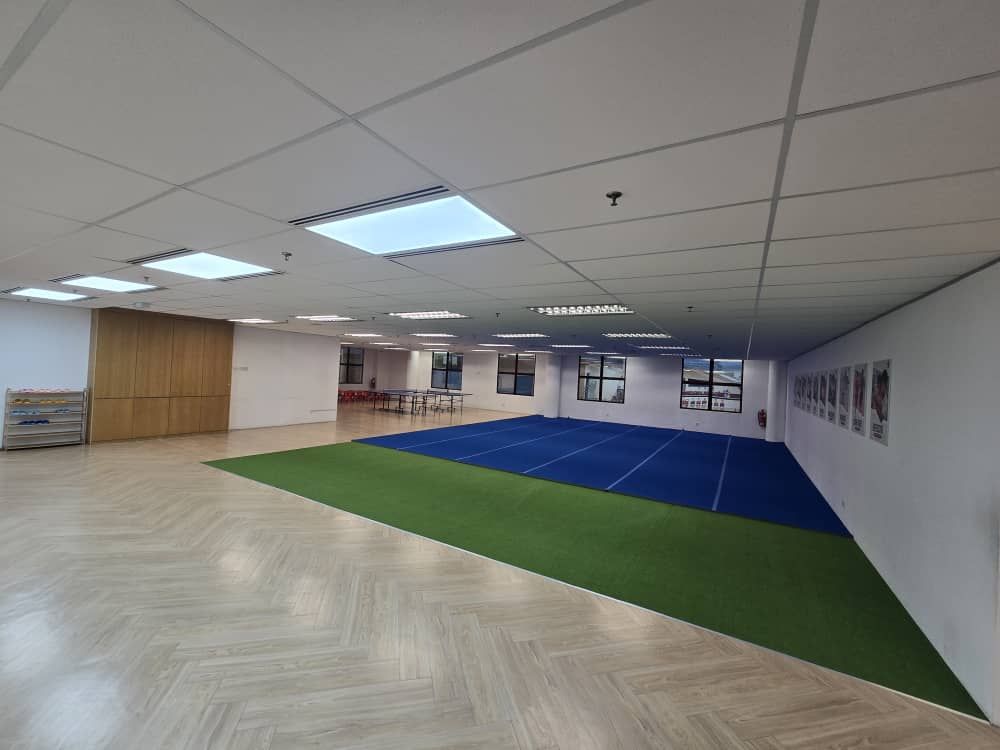 Indoor room with wooden floor, green and blue mats, white walls, and rectangular ceiling lights.