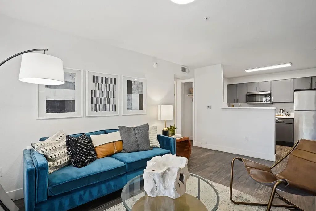 Living room in an apartment with a blue sofa, abstract wall art, and an open kitchen.