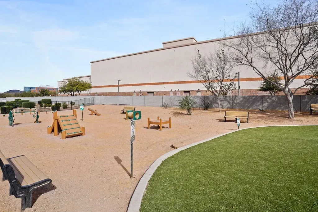 Outdoor playground with wooden play structures, benches, and a curved grass edge beside a large building.