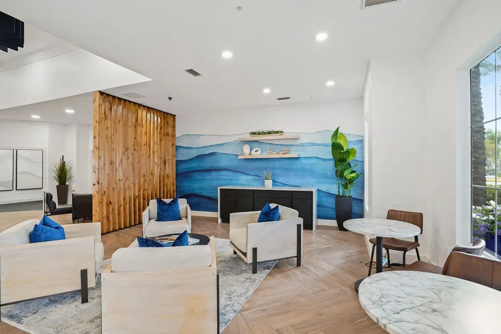 Indoor community lounge with a blue wave mural, seating and marble tables.