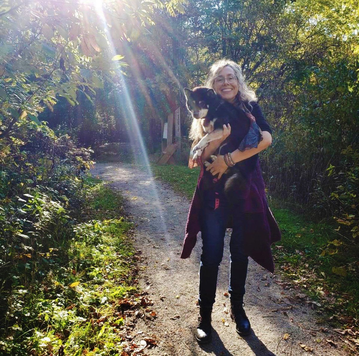 A woman is holding a dog on a path in the woods