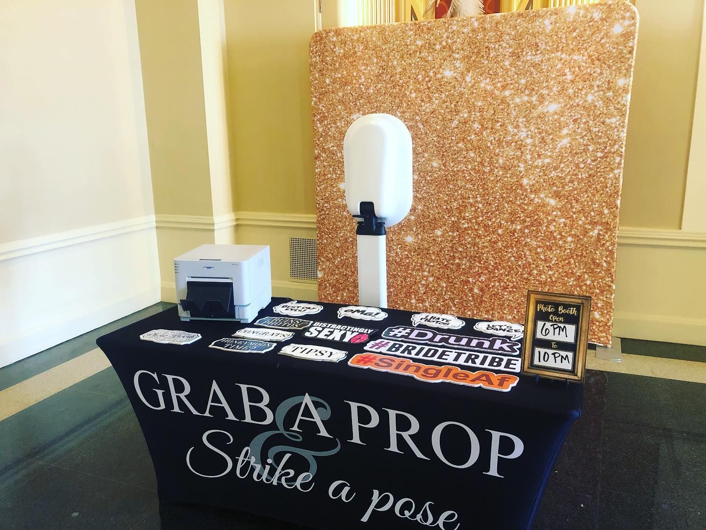 Photo booth setup with gold glitter backdrop, props, and printer on a 