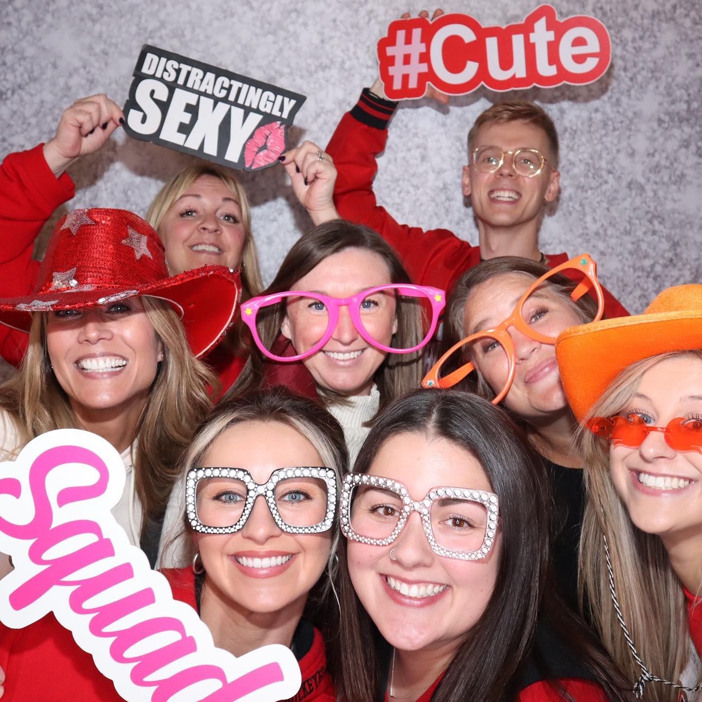 Group photo booth picture with eight people wearing props; holding signs, smiling at camera.