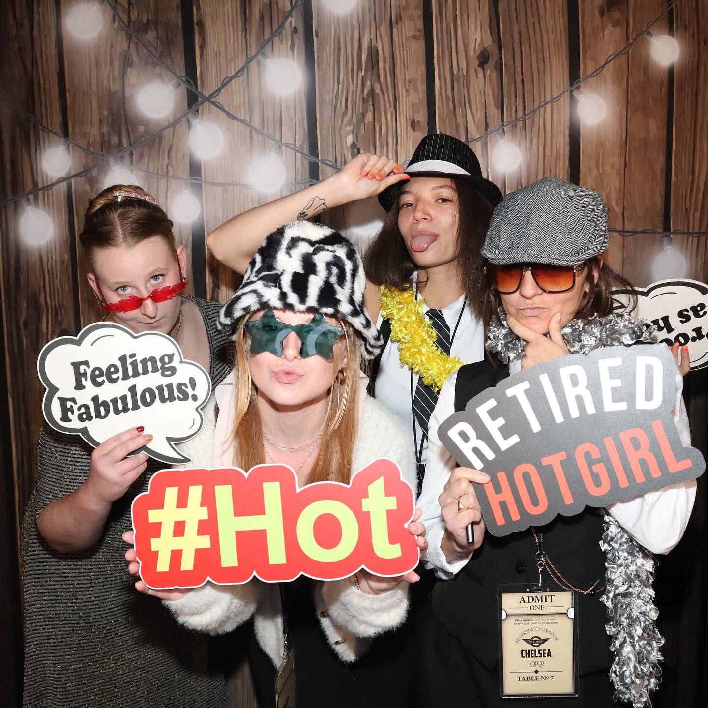 Four people posing in photo booth, holding props. One says 