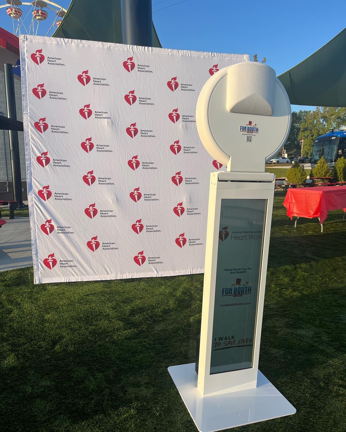Photo booth with an American Heart Association backdrop outdoors on grass.