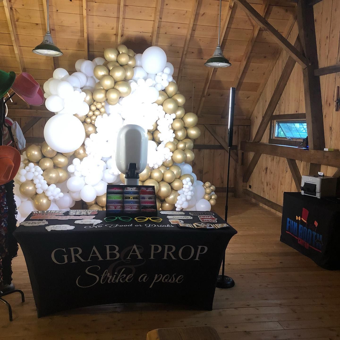 Photo booth setup at an event, with balloon backdrop in gold and white, props table, and black tablecloth.