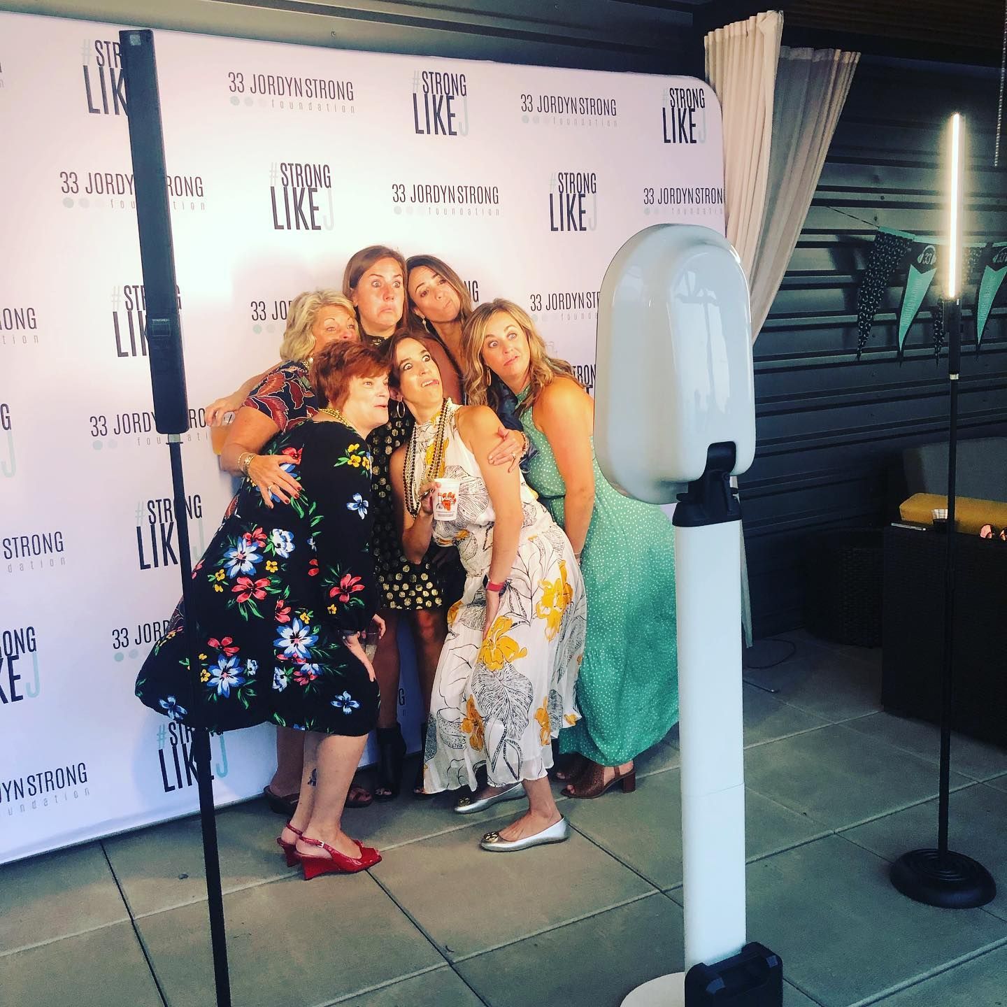 Group of people posing for a photo booth. They are smiling and embracing against a branded backdrop.