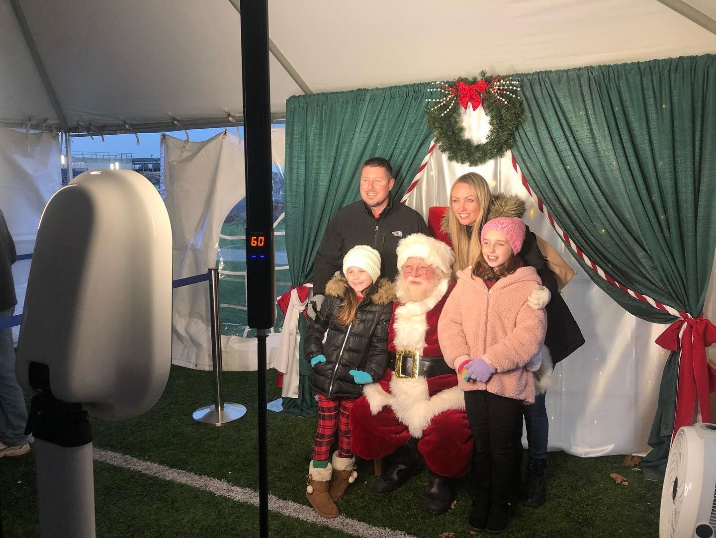 Family with Santa in front of a Christmas backdrop. Photo booth with white casing in the foreground.