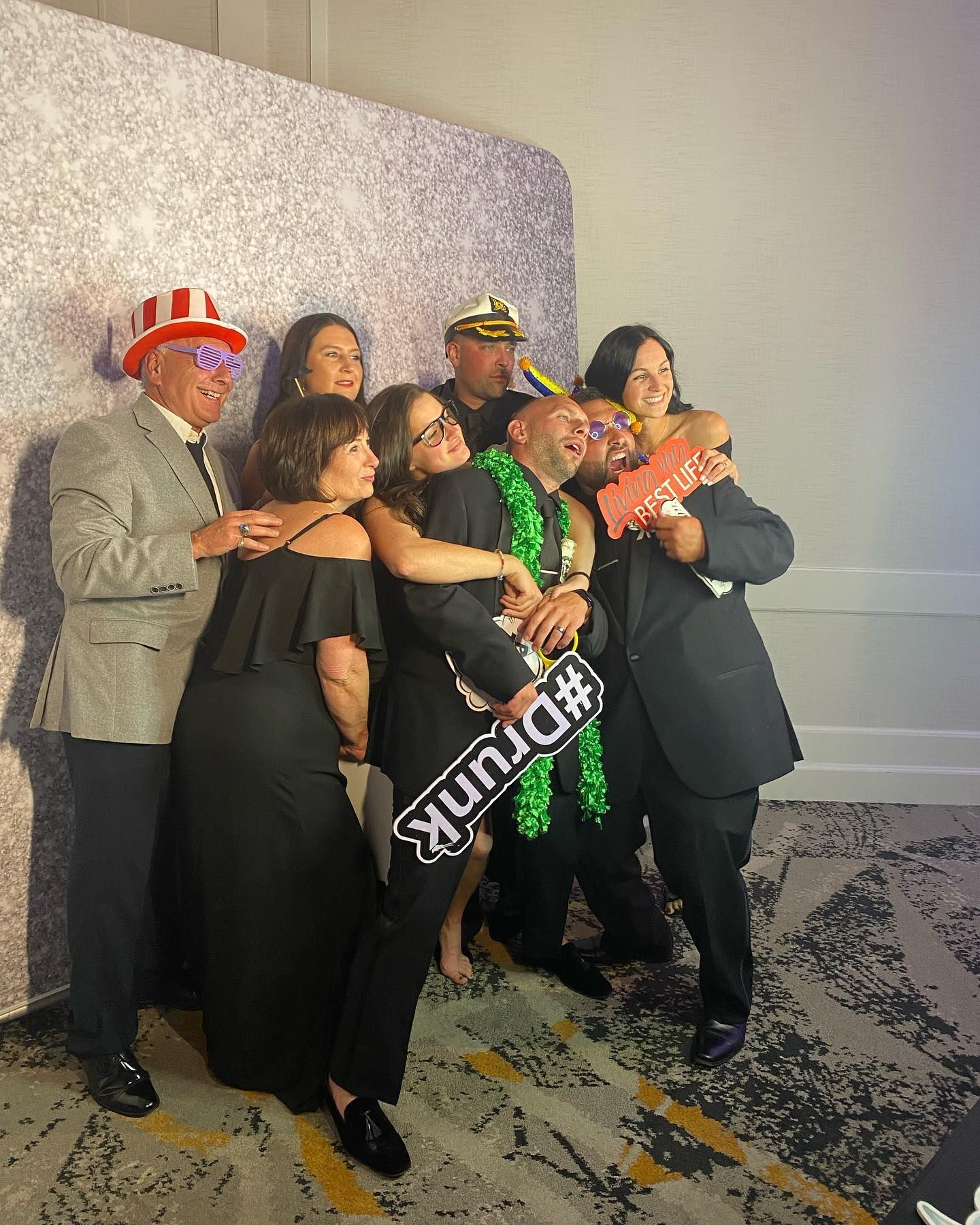 Group of people pose for photo at a party, some wearing festive hats and holding a prop that says #Drunk.