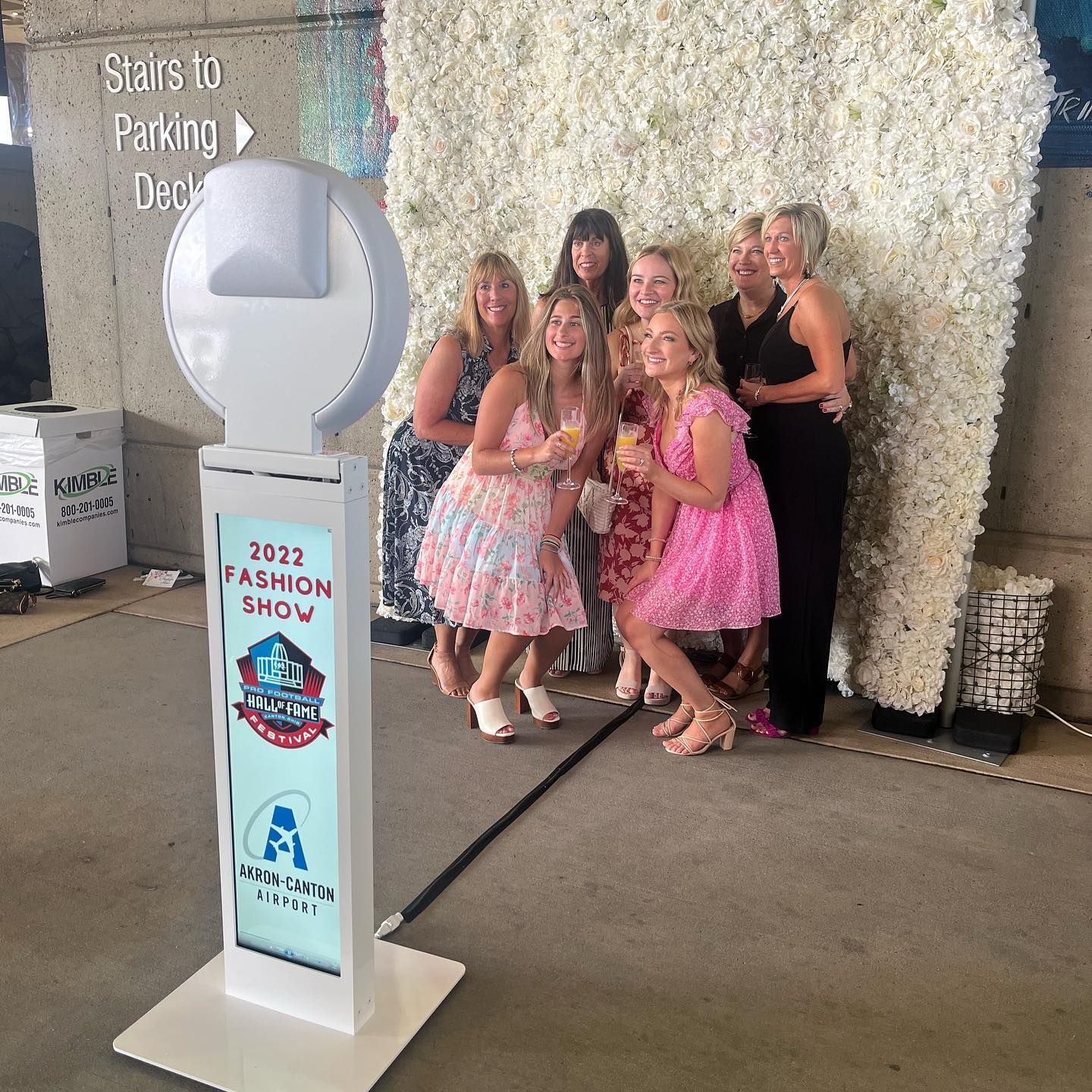 Photo booth with a group of women posing in front of a flower wall at a fashion show.