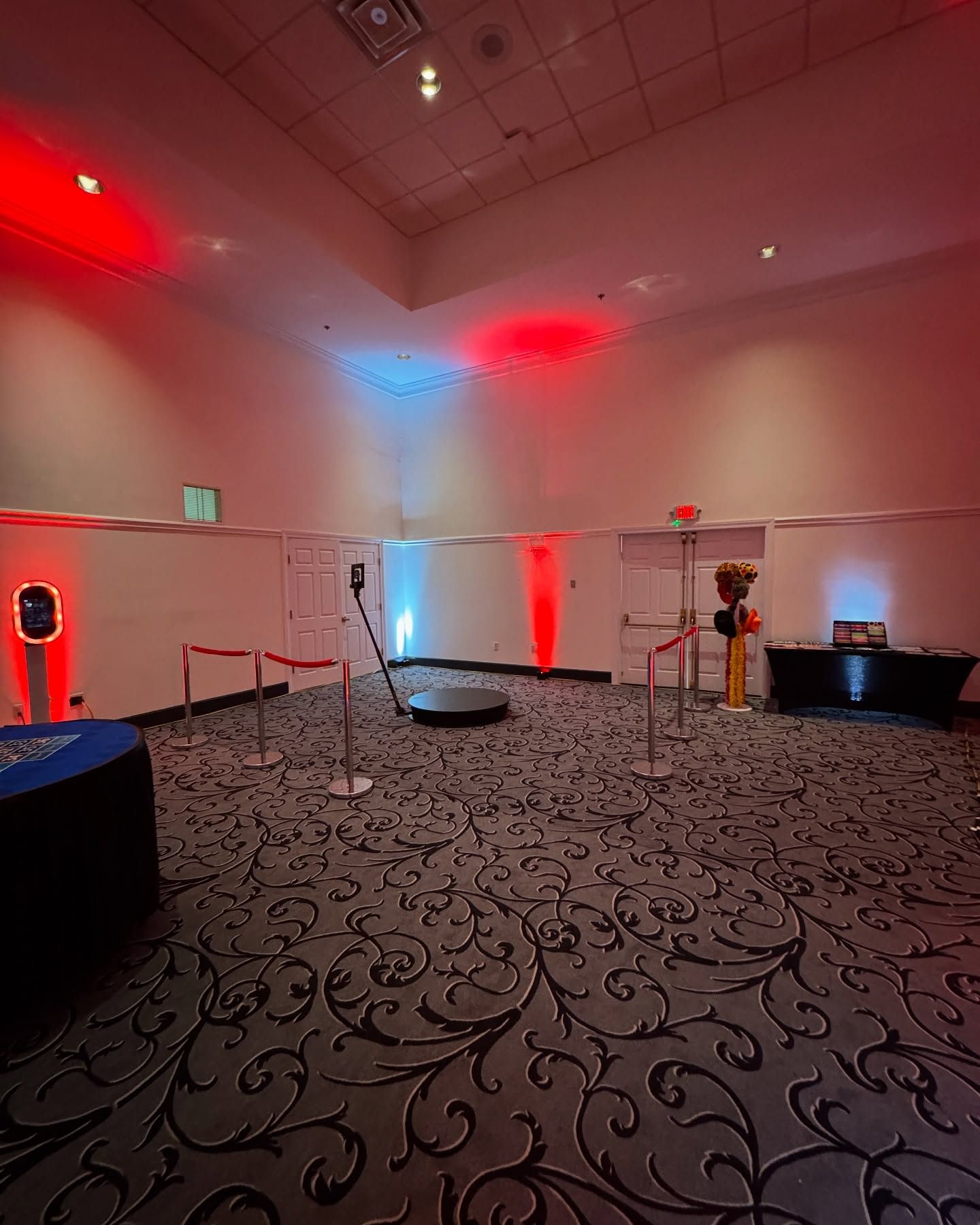 Event space with a 360 photo booth setup, red and blue lighting, and stanchions.