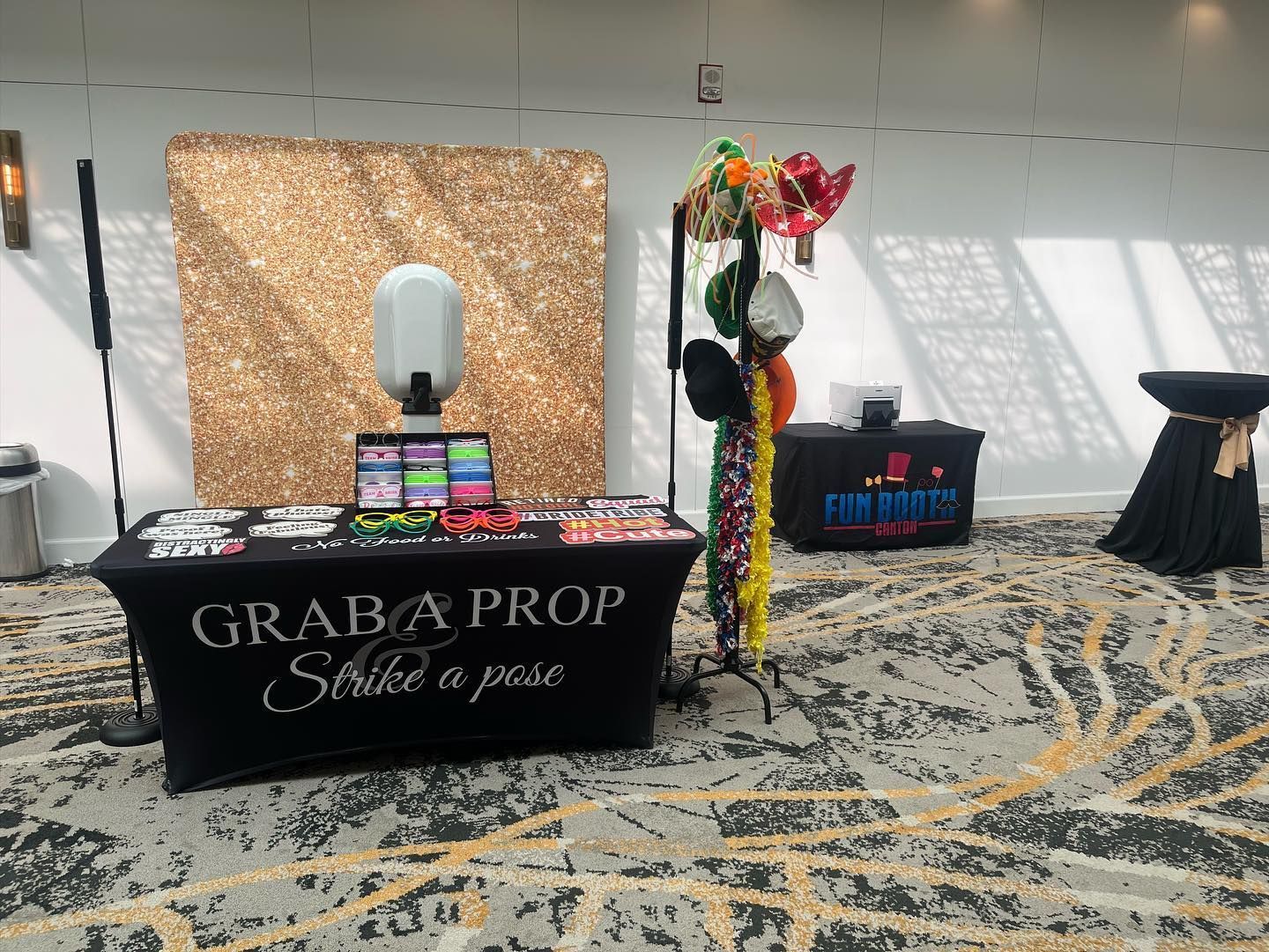 Photo booth setup with gold backdrop, props, and black table cover that says 