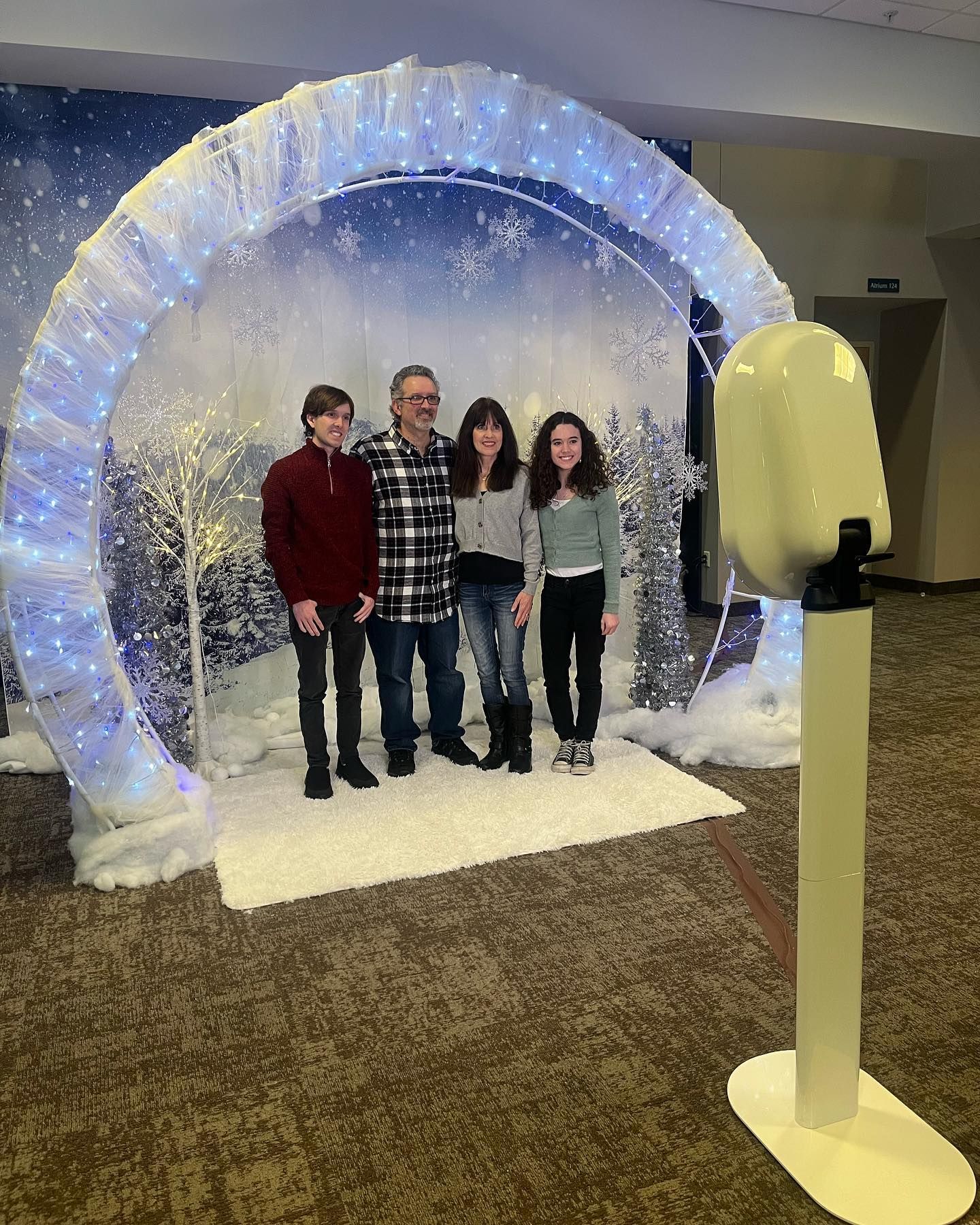 Family posing in front of a winter-themed photo booth archway. A white photo booth camera stands to the side.