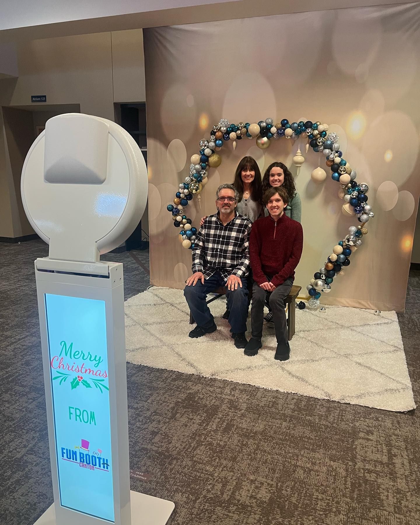 Family posing for photo by a photo booth at an event. Decorated backdrop with lights and garland.