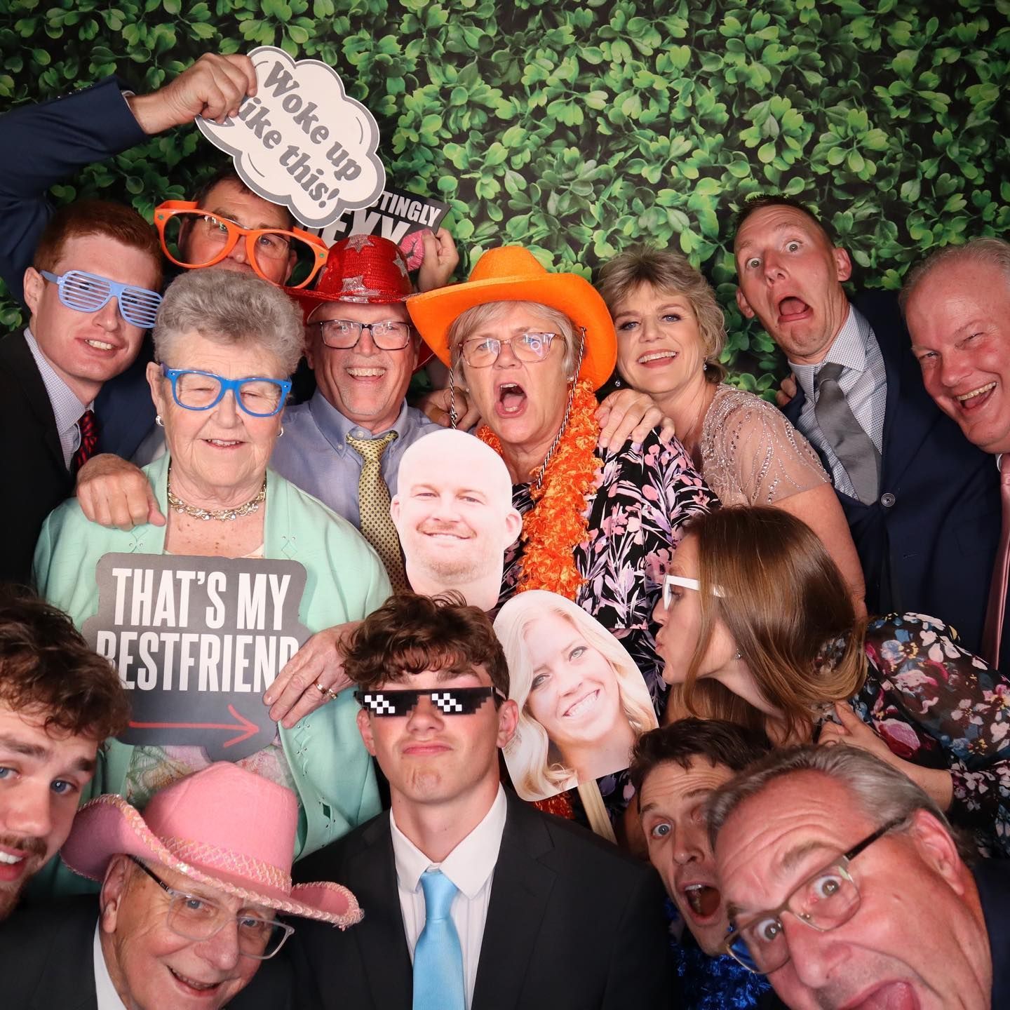 Group photo booth shot with people holding props, making silly faces. Green backdrop.