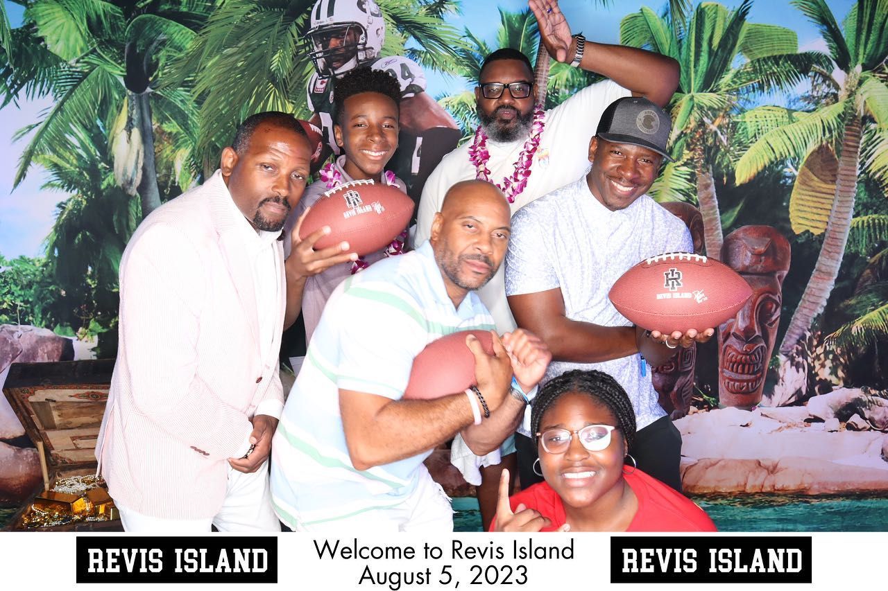 Group of people posing with footballs in front of a tropical backdrop, celebrating at 