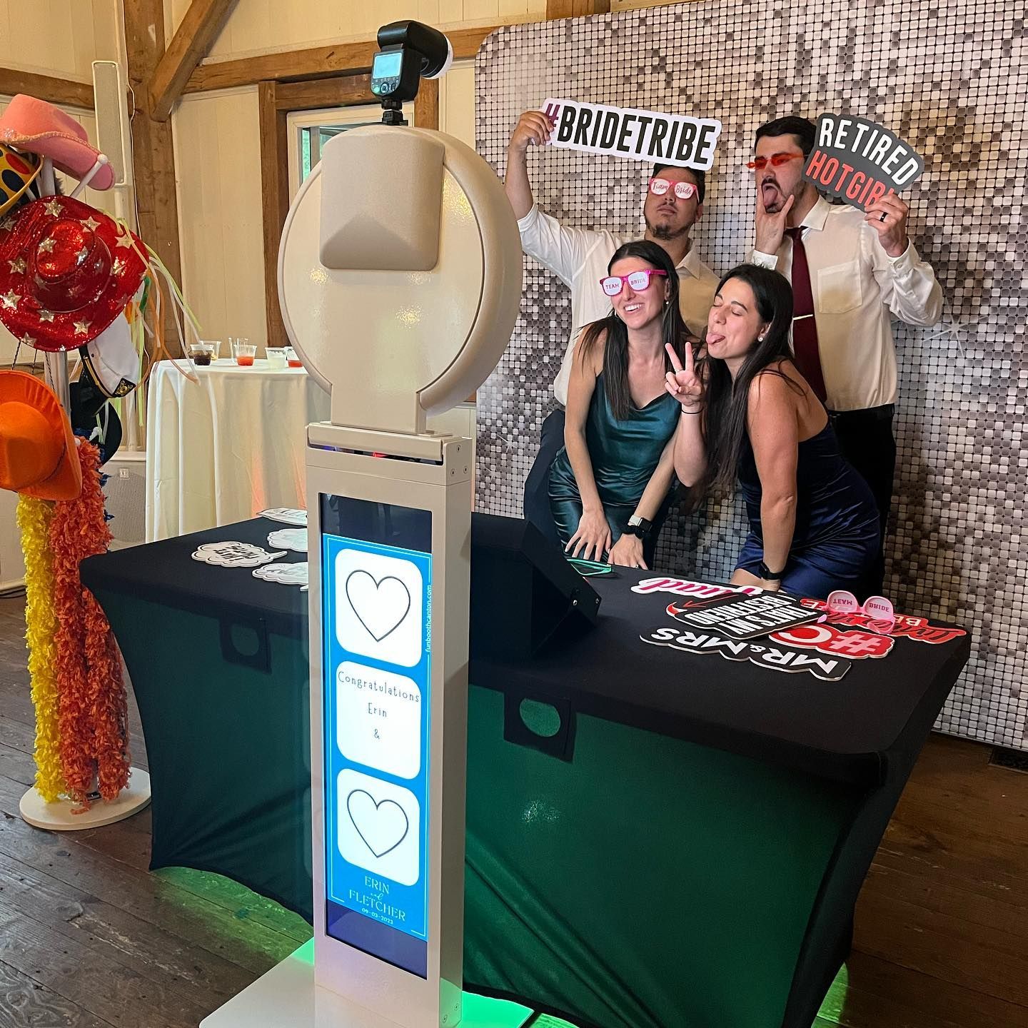 Photo booth at a party with four people posing with props in front of a backdrop; two women, two men.