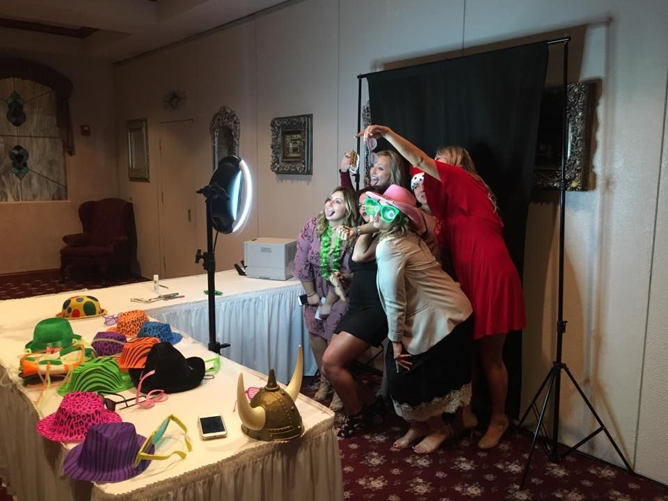 People pose for a photo at a photo booth with props, black backdrop, and ring light.
