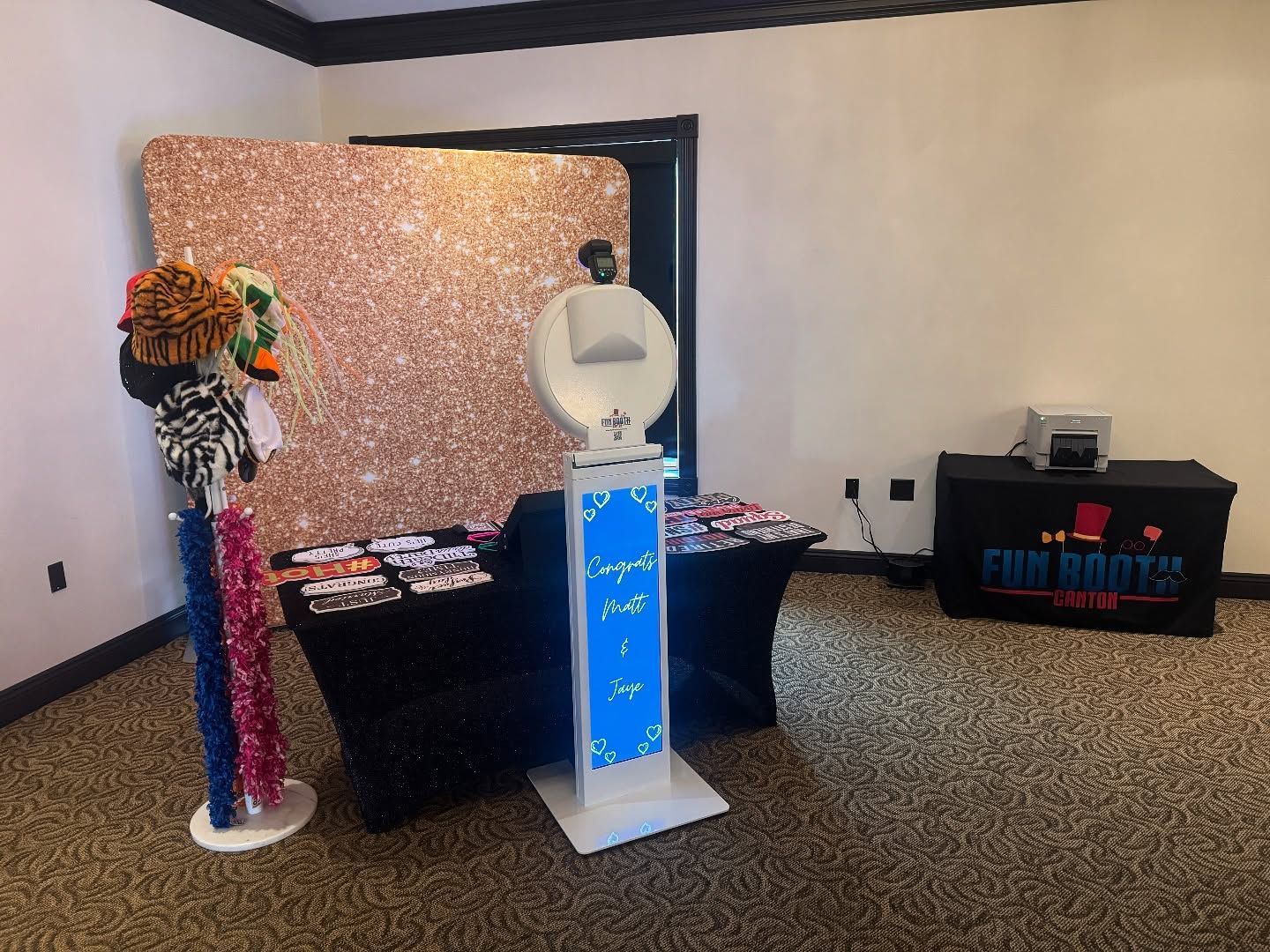 Photo booth set up at an event with a rose gold backdrop, props, and a table with Fun Booths logo.