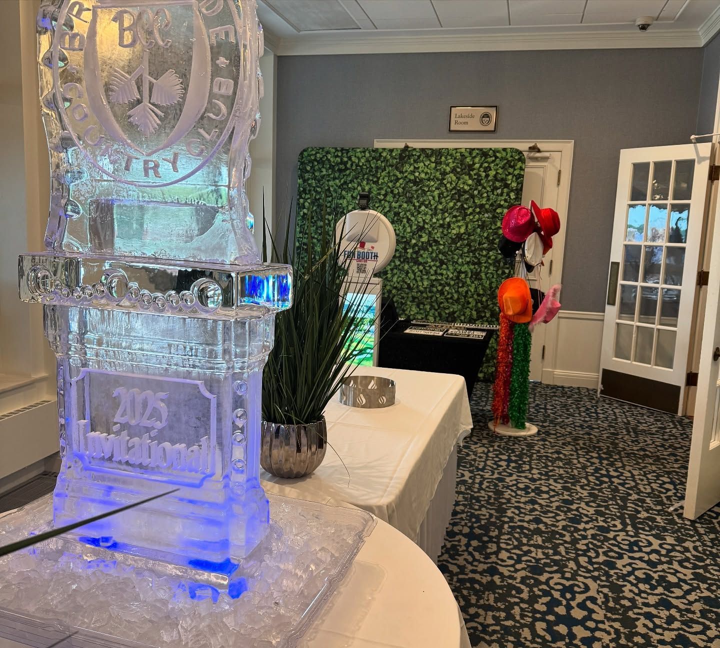 Ice sculpture with blue lights, table set up for an event, greenery wall, open doors.