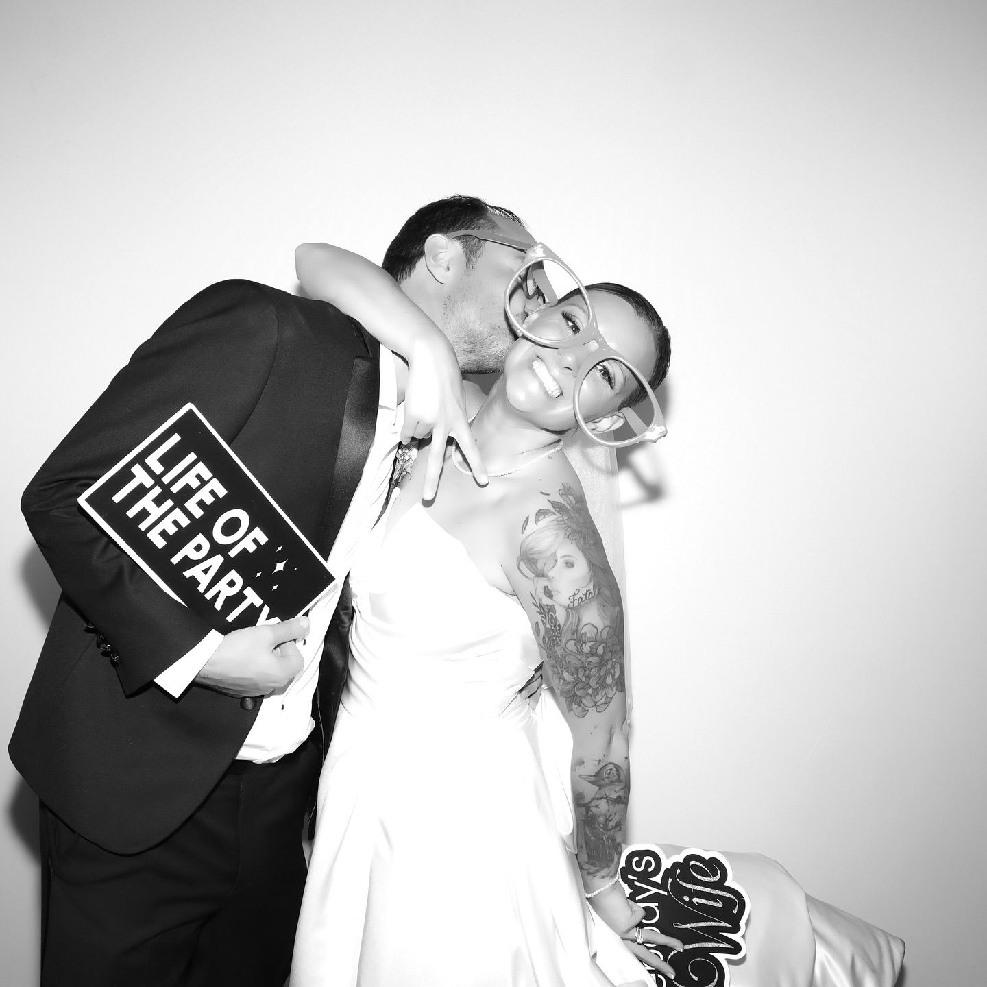 Couple posing for a photo booth. Man kissing woman on the cheek, holding a 