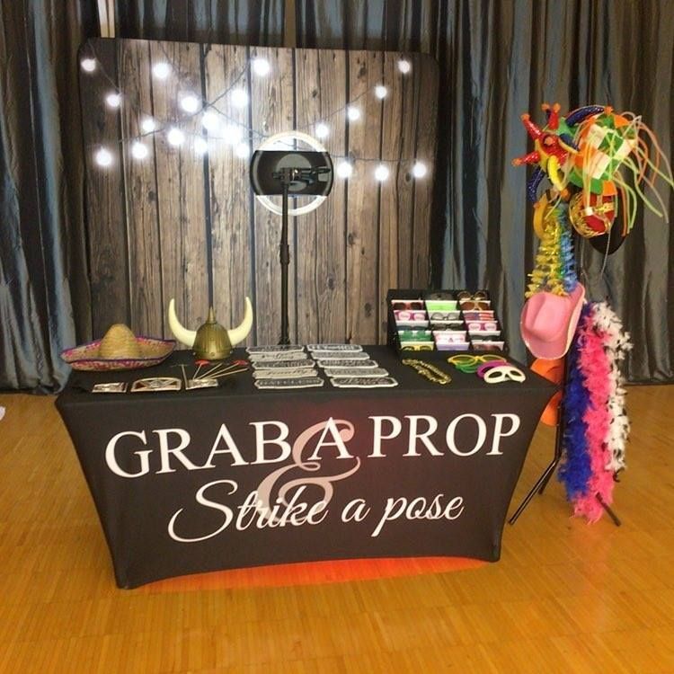 Photo booth setup with props: backdrop, camera, prop table with accessories, and a rack of items.