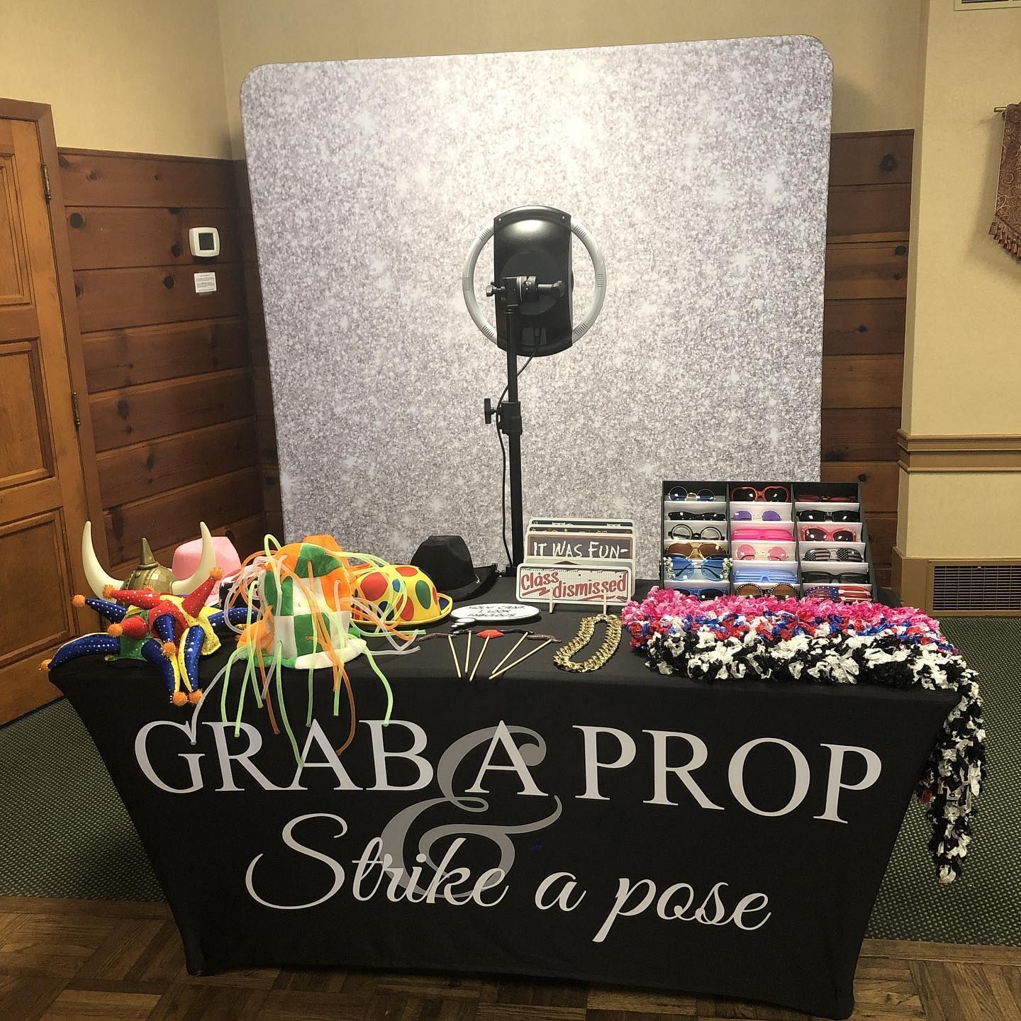 Photo booth setup with props like hats and leis, in front of a textured backdrop.