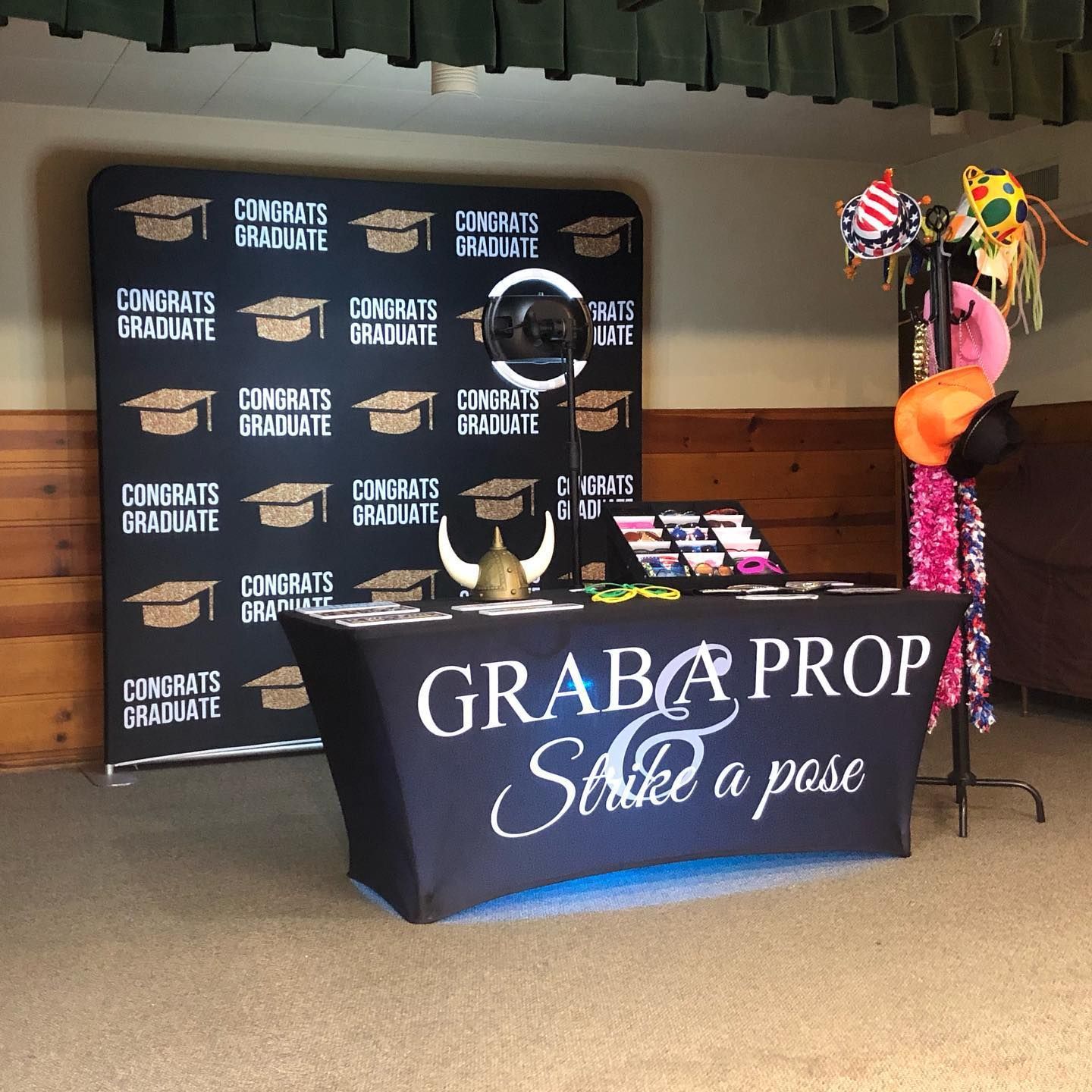 Photo booth setup with graduation backdrop and props. Table displays 