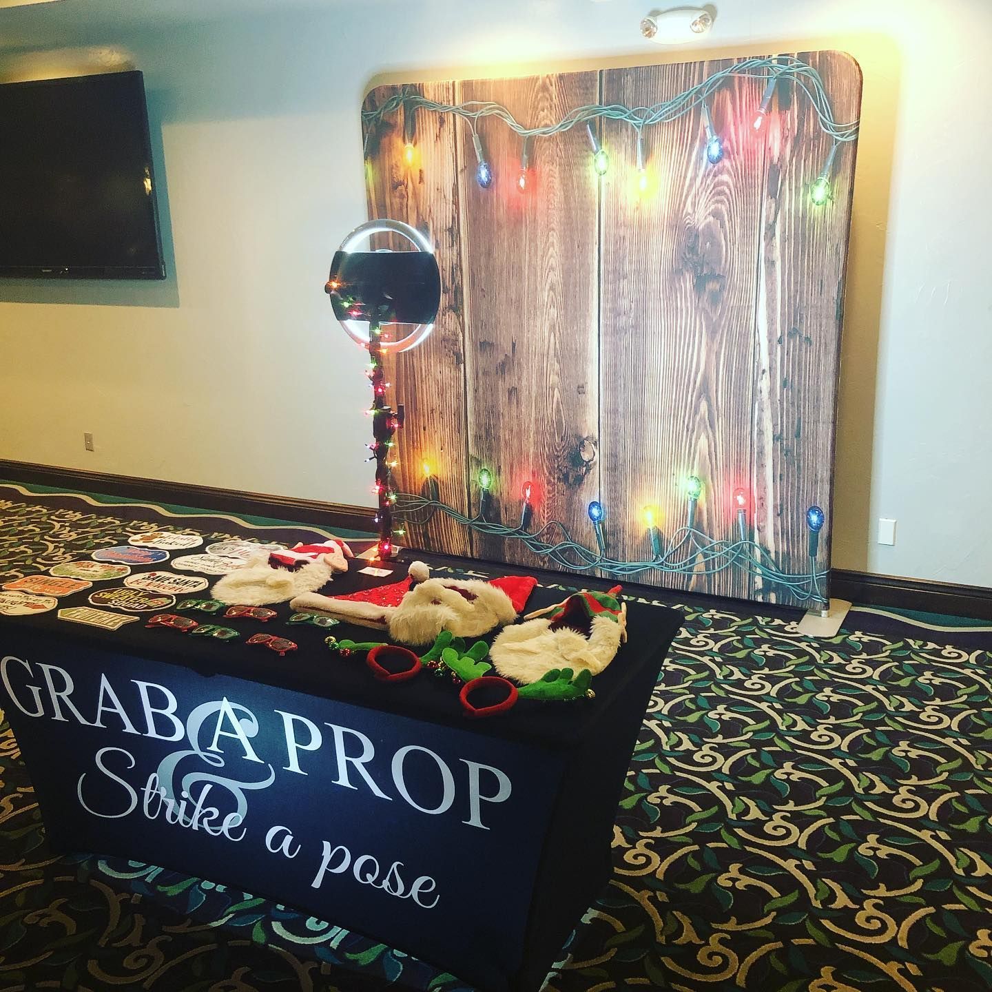 Photo booth setup with wooden backdrop, props, and a sign encouraging guests to 